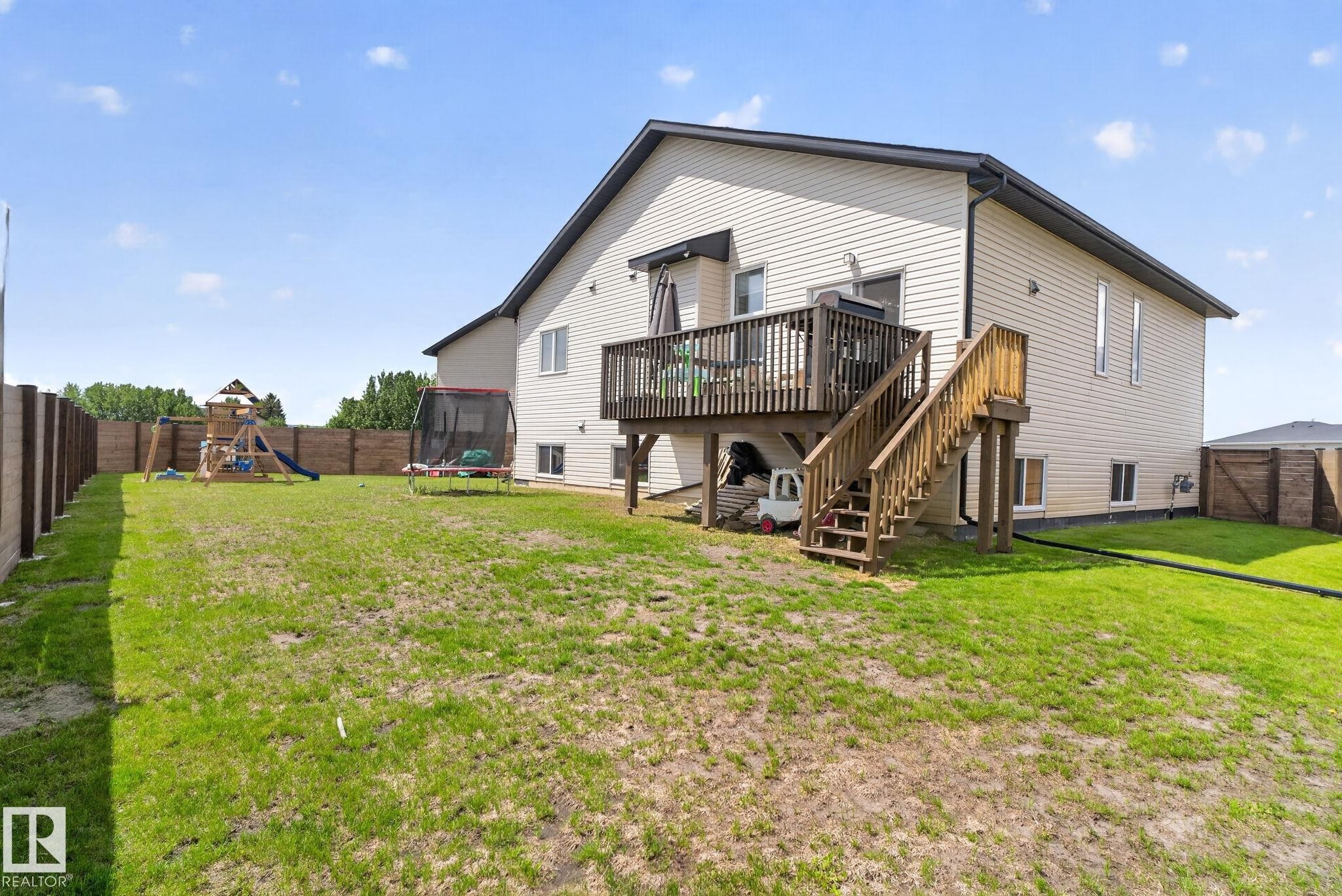 Expansive backyard featuring a wood deck with stairs, a cream-colored siding exterior, and a privacy fence - 4204 55Av, Lamont, AB