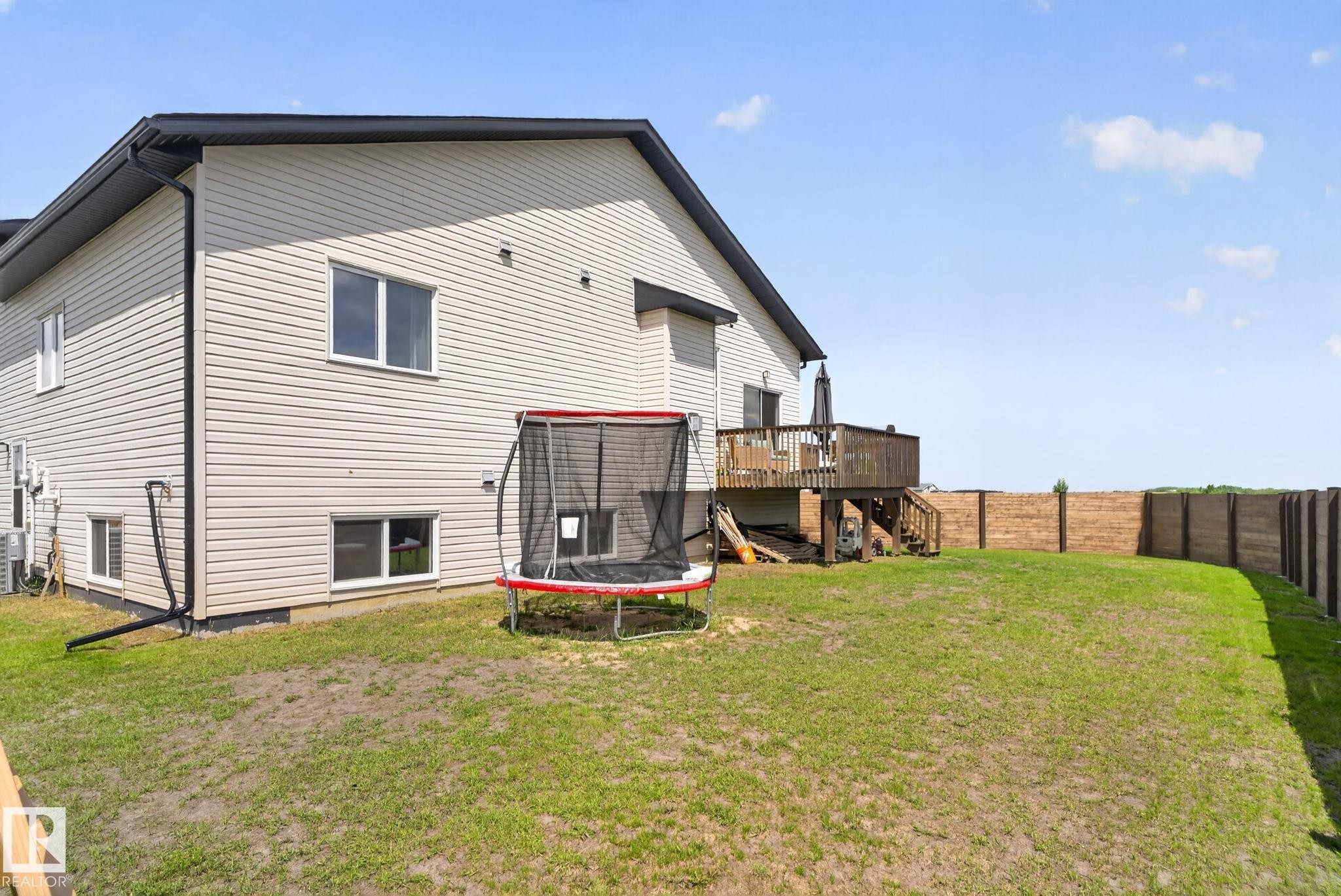 Rear exterior featuring light-colored siding, a dark wood-finish deck with railing, and a privacy fence enclosing the yard - 4204 55Av, Lamont, AB