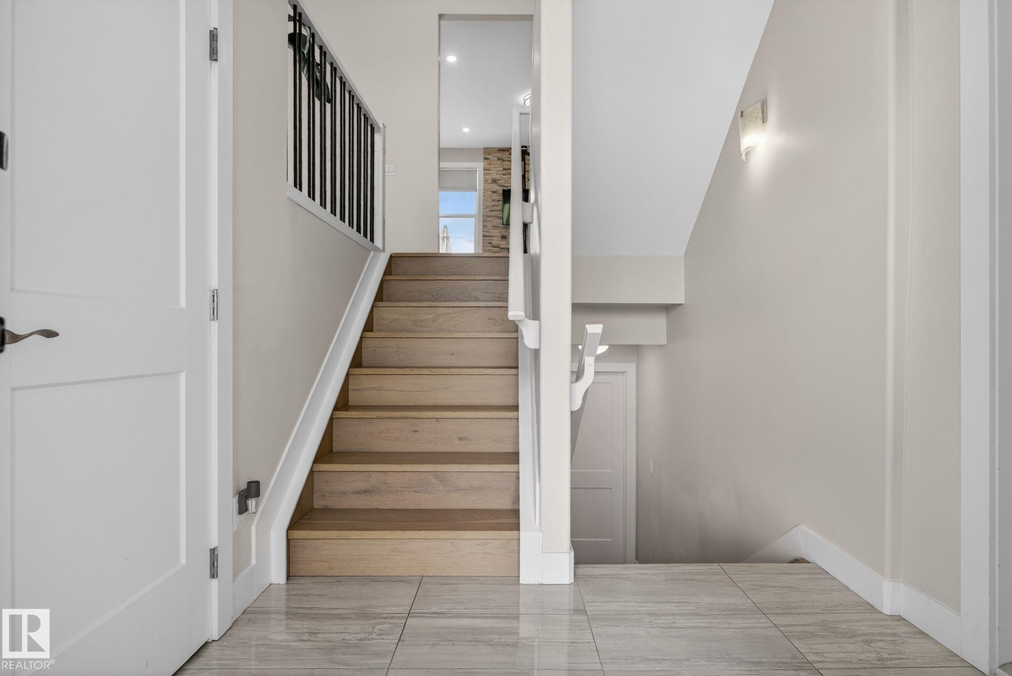Entryway featuring large format grey tile flooring, wood-finish stairs with white risers, and black metal balusters - 4204 55Av, Lamont, AB