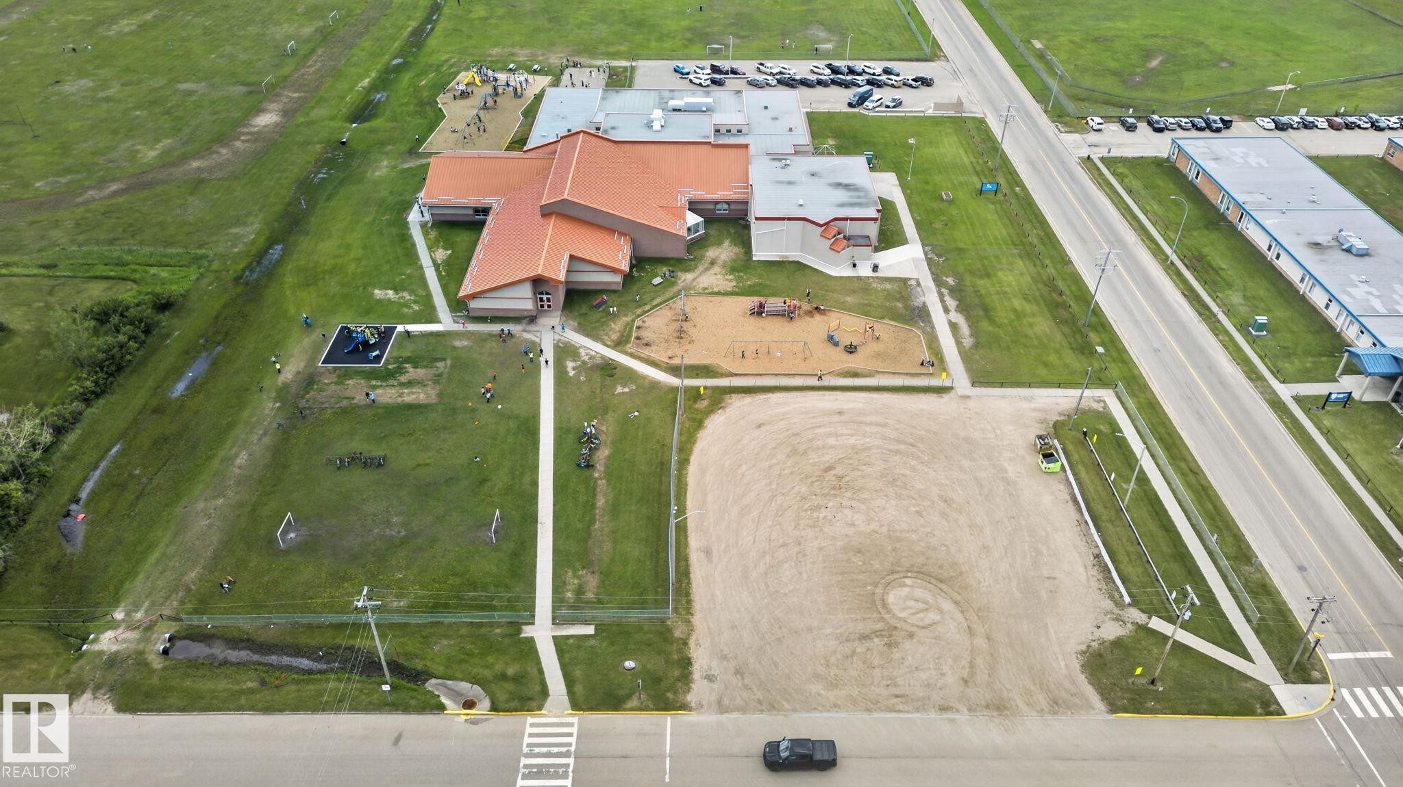 Spacious property featuring a large building with a terracotta-toned roof, multiple paved parking areas, extensive grassy fields, and two distinct playground structures - 4204 55Av, Lamont, AB