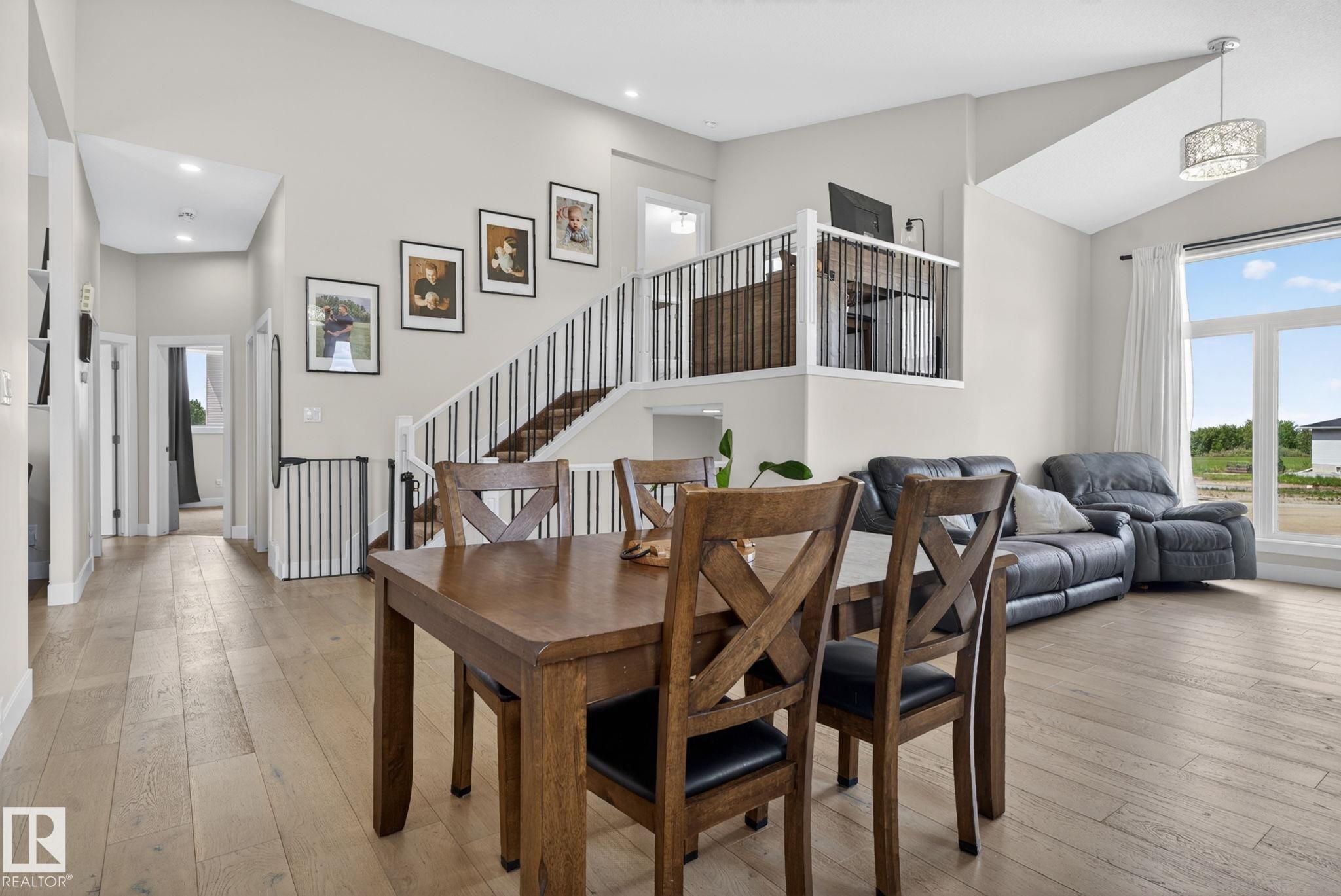 Open-concept interior featuring light wood-finish flooring, a contemporary staircase with white risers and dark balusters, vaulted ceilings, and large windows with white trim - 4204 55Av, Lamont, AB