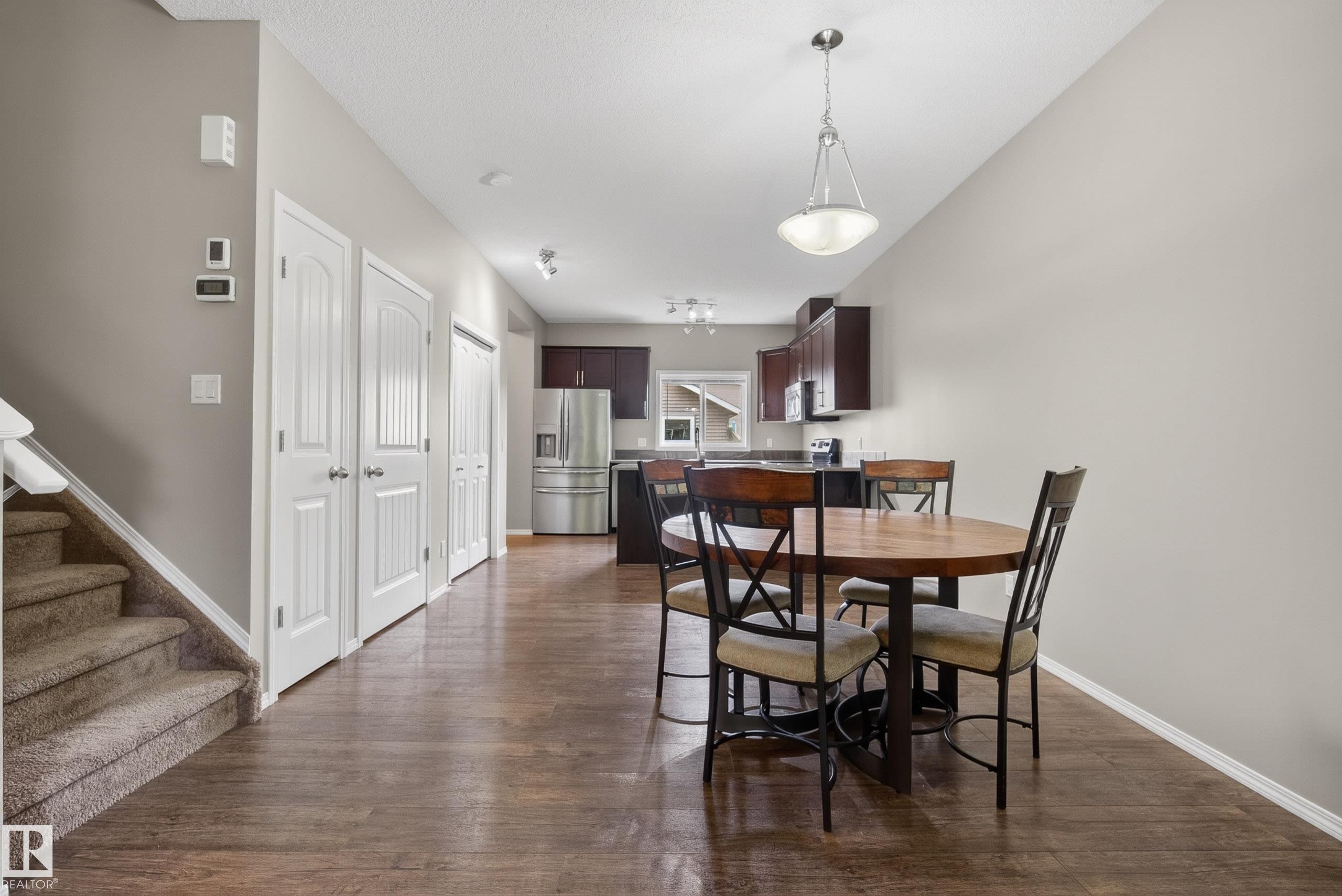 Open-concept living space featuring wood-finish flooring, a kitchen with dark cabinetry, stainless steel appliances, and a central dining area with pendant lighting - 2325 69A Street, Edmonton, AB