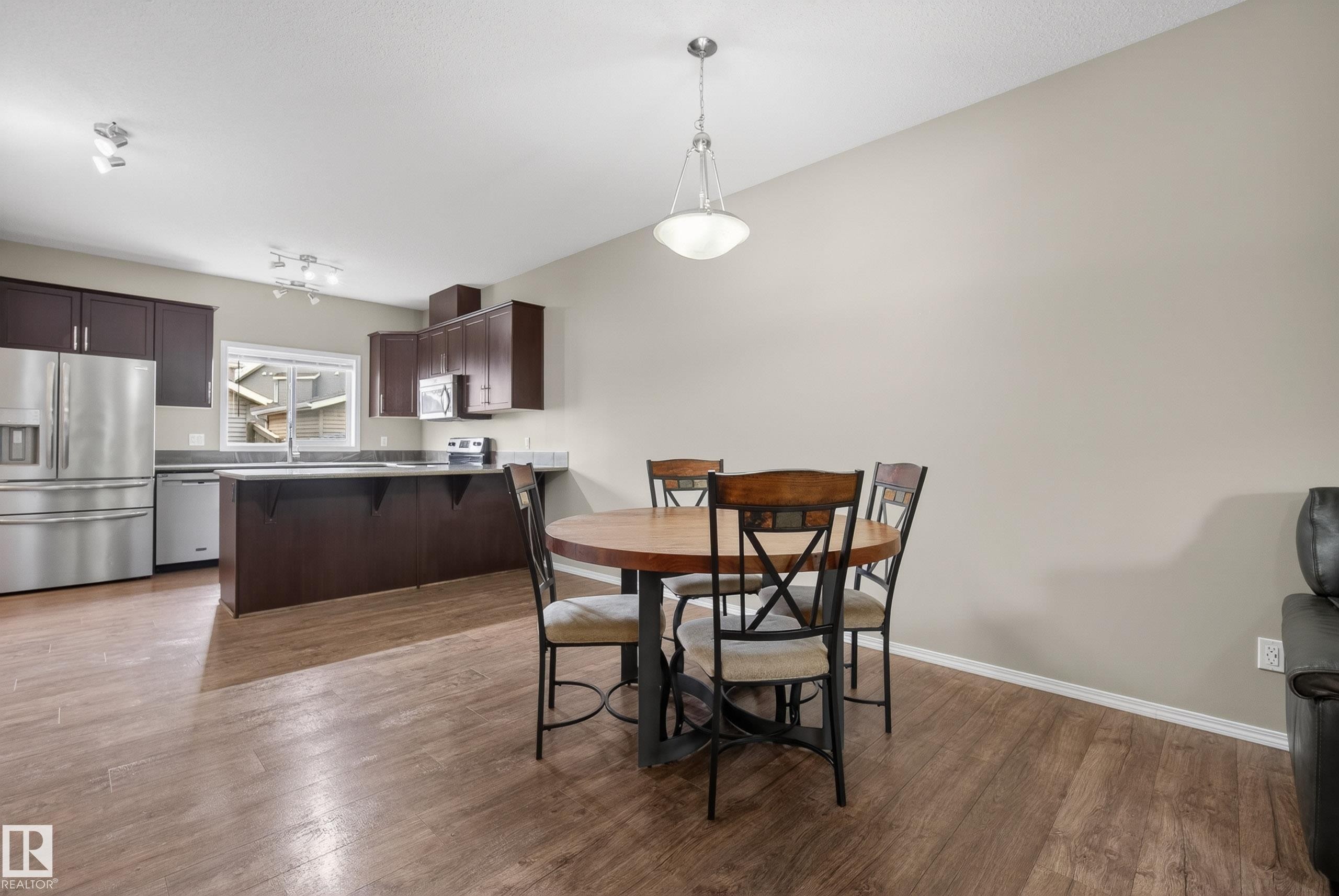 Open-concept kitchen and dining area featuring wood-finish flooring, dark wood cabinetry, stainless steel appliances, and a window above the sink - 2325 69A Street, Edmonton, AB