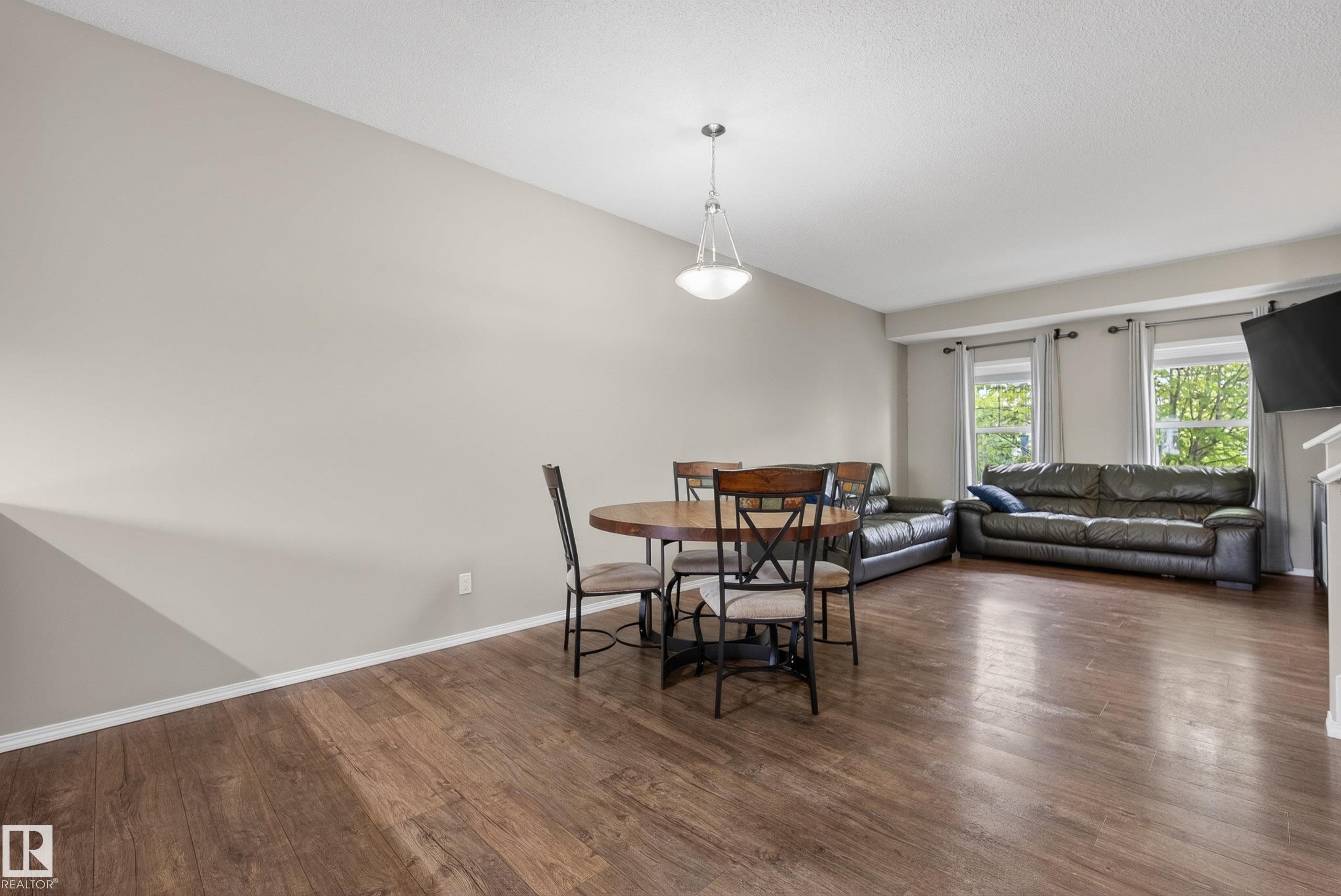 Open-concept living area featuring wood-finish flooring, recessed windows with natural light, and a contemporary ceiling fixture - 2325 69A Street, Edmonton, AB