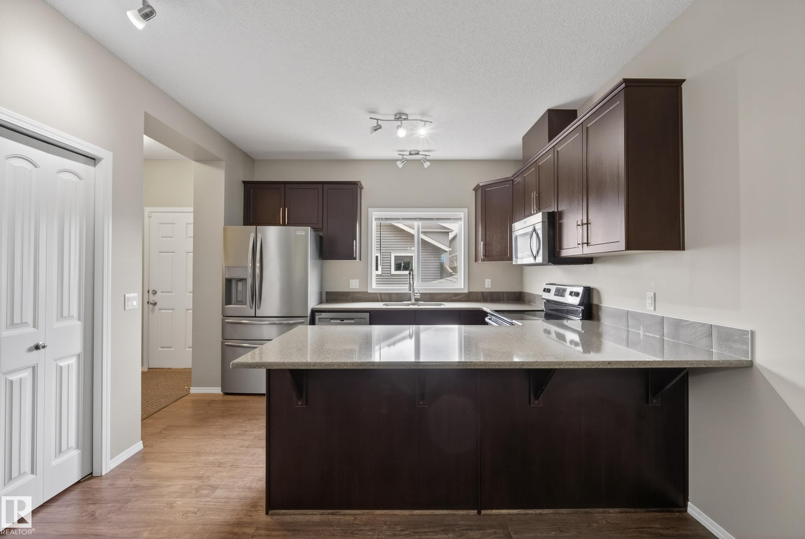 Kitchen featuring wood-finish flooring, dark wood cabinetry, and light-toned countertops - 2325 69A Street, Edmonton, AB