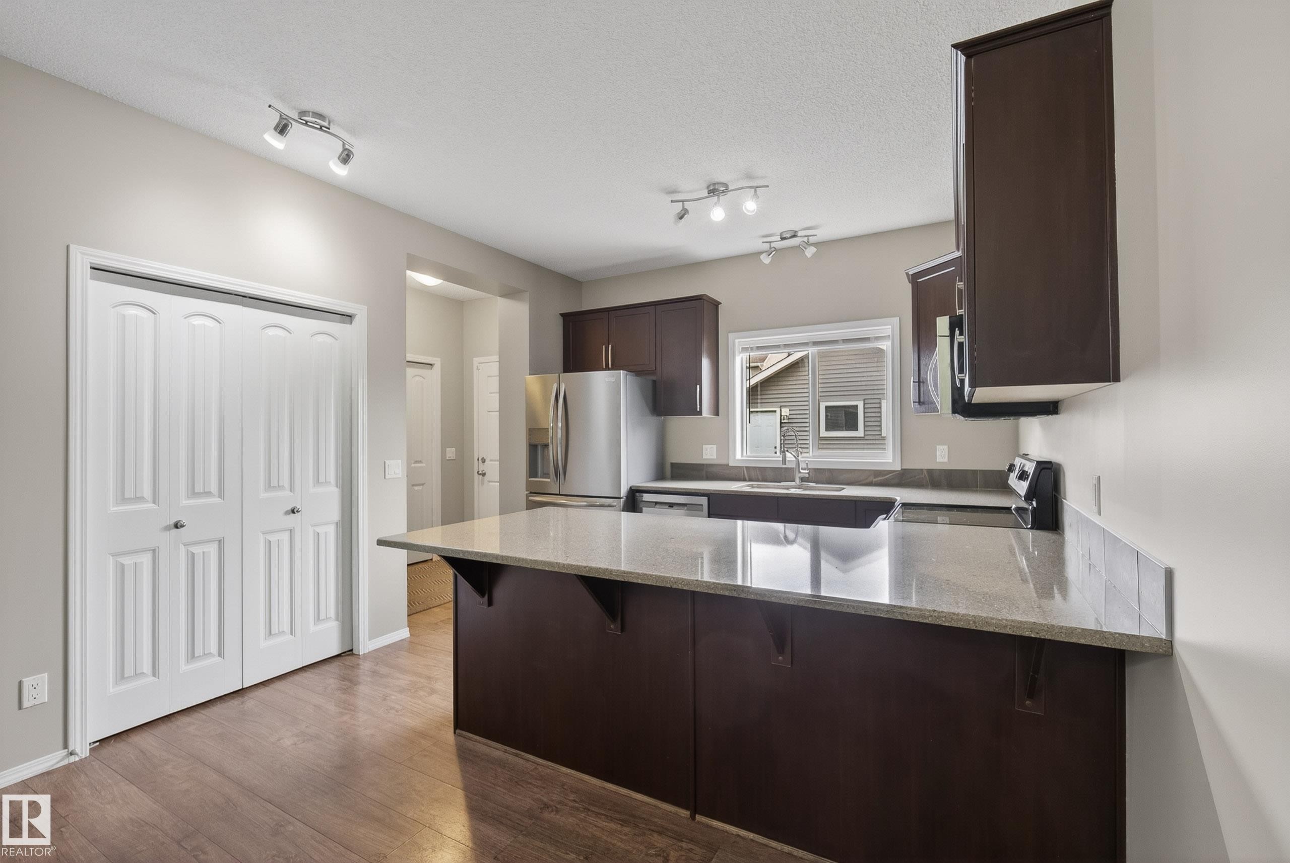 Kitchen featuring wood-finish flooring, dark wood cabinetry, light-toned countertops, and stainless steel appliances - 2325 69A Street, Edmonton, AB