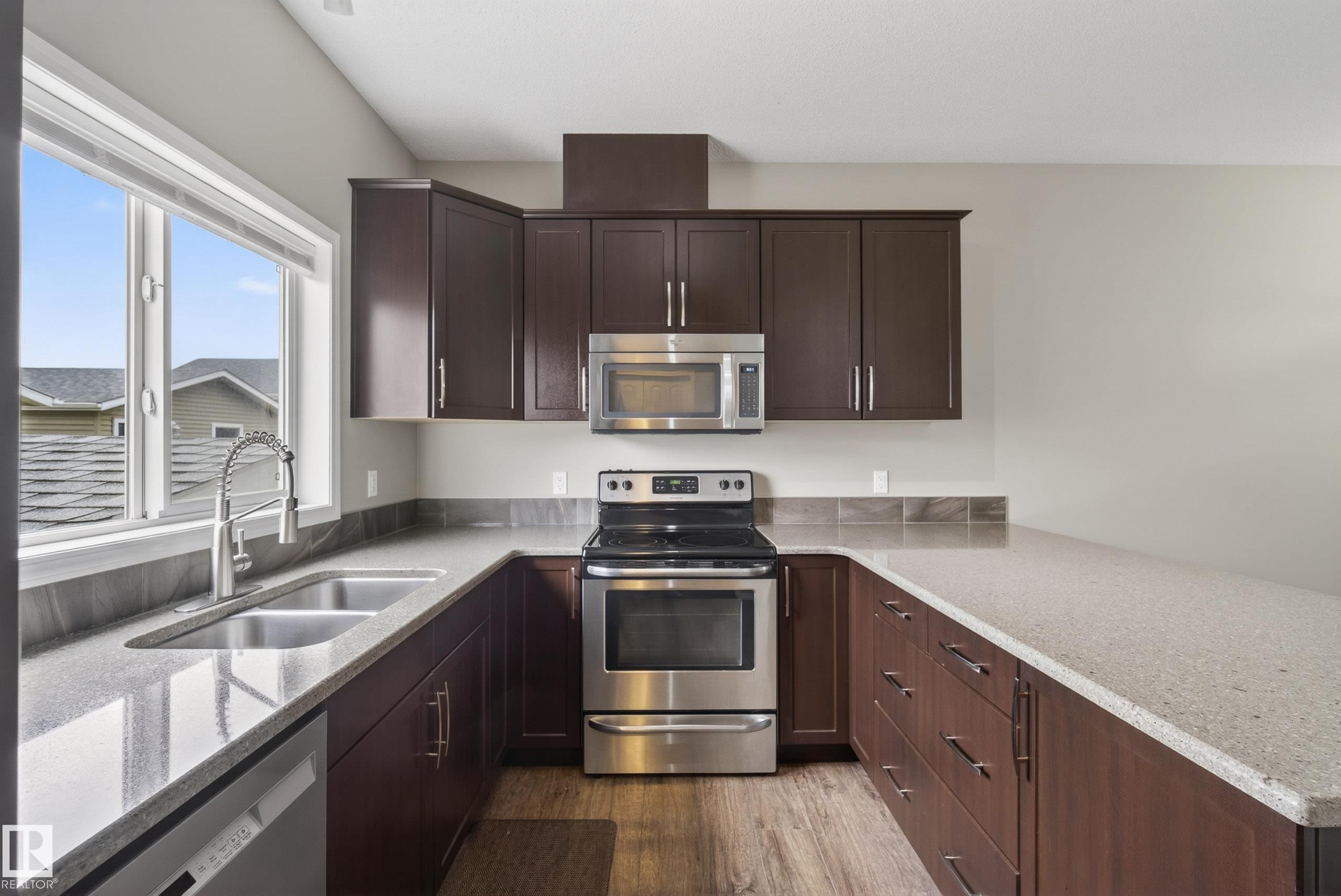 U-shaped kitchen featuring dark wood cabinetry, light-toned countertops, and stainless steel appliances - 2325 69A Street, Edmonton, AB