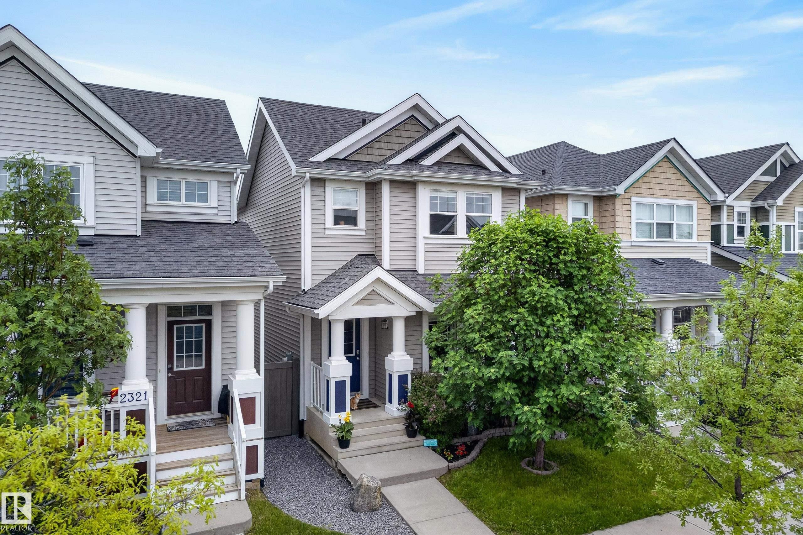 Townhome exterior featuring light gray siding, dark gray shingle roofing, white-trimmed windows, and a covered front porch with white columns - 2325 69A Street, Edmonton, AB