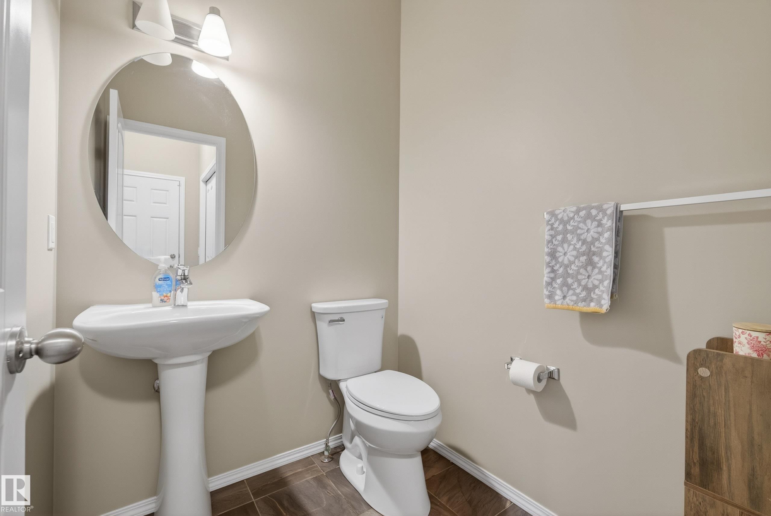 Pedestal sink featuring a round mirror and overhead lighting - 2325 69A Street, Edmonton, AB