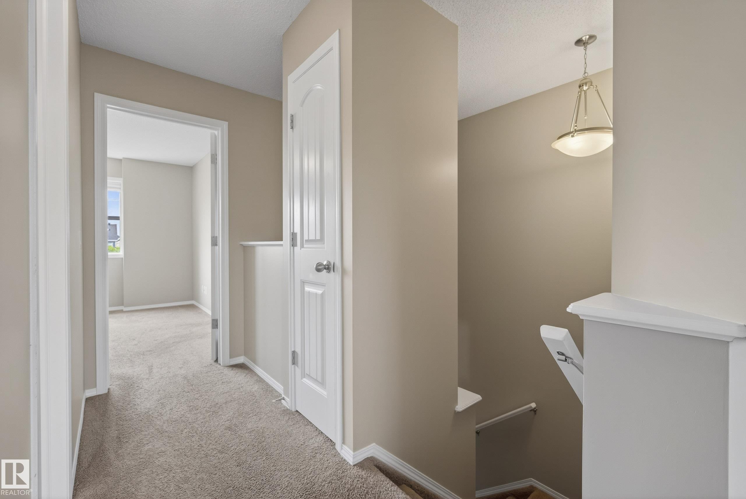 Upper-level landing featuring neutral paint, textured carpeting, white trim, and a semi-flush mount ceiling light fixture - 2325 69A Street, Edmonton, AB