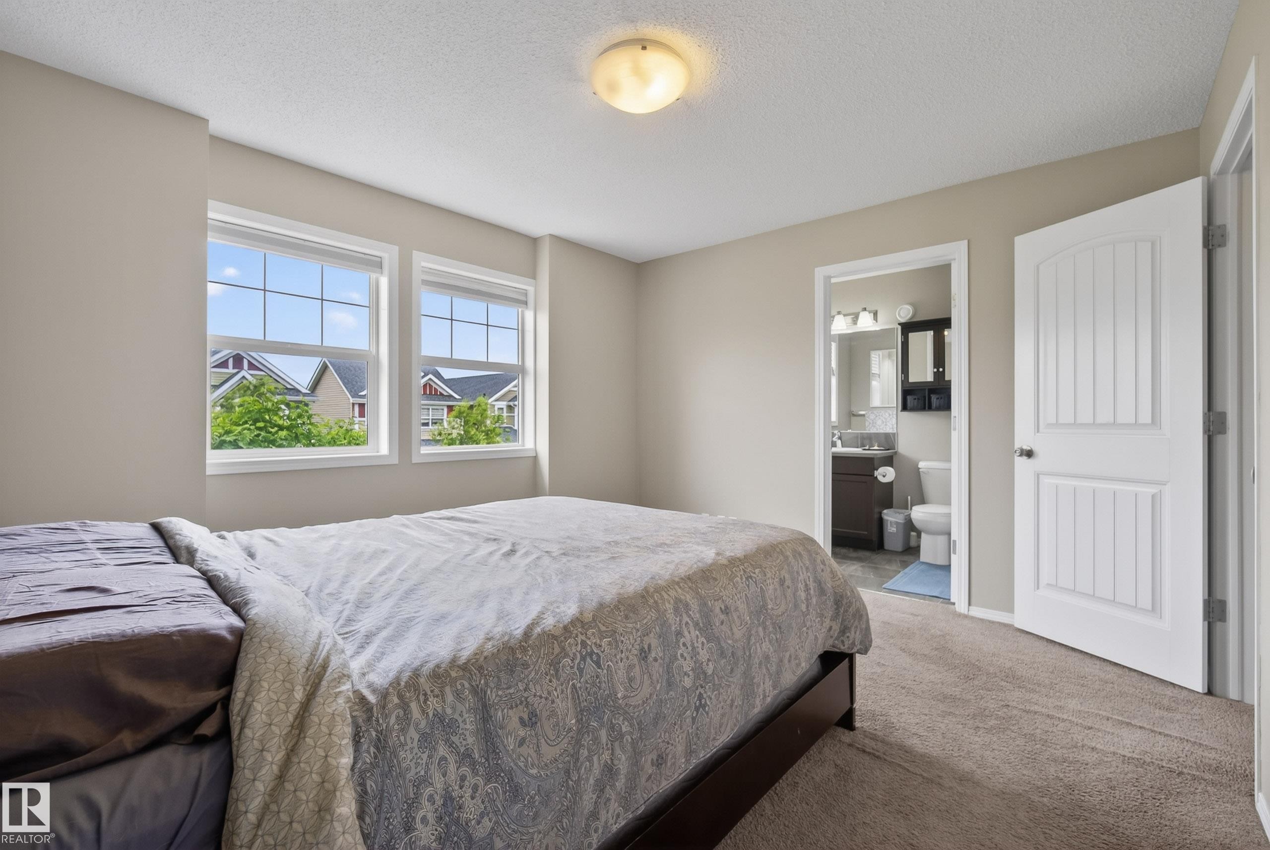 Carpeted bedroom featuring two large windows, a ceiling-mounted light fixture, and a paneled door - 2325 69A Street, Edmonton, AB