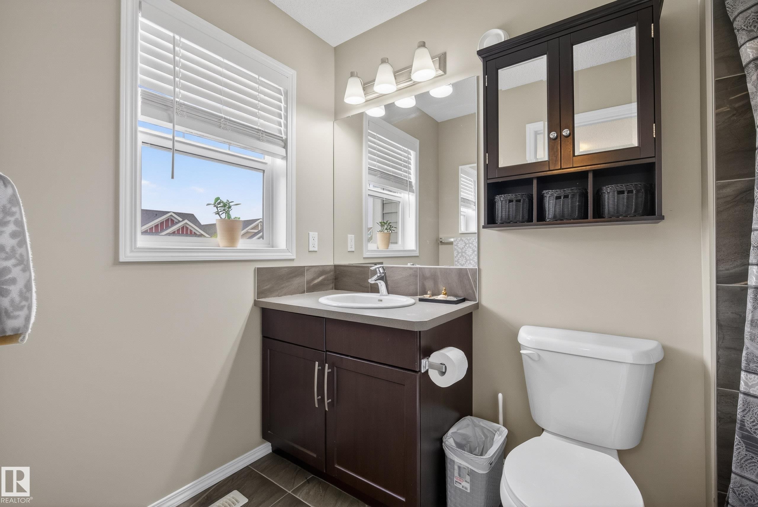 Bathroom featuring a dark wood-finish vanity with a white basin sink and light countertop, complemented by a large mirror and three-light fixture - 2325 69A Street, Edmonton, AB