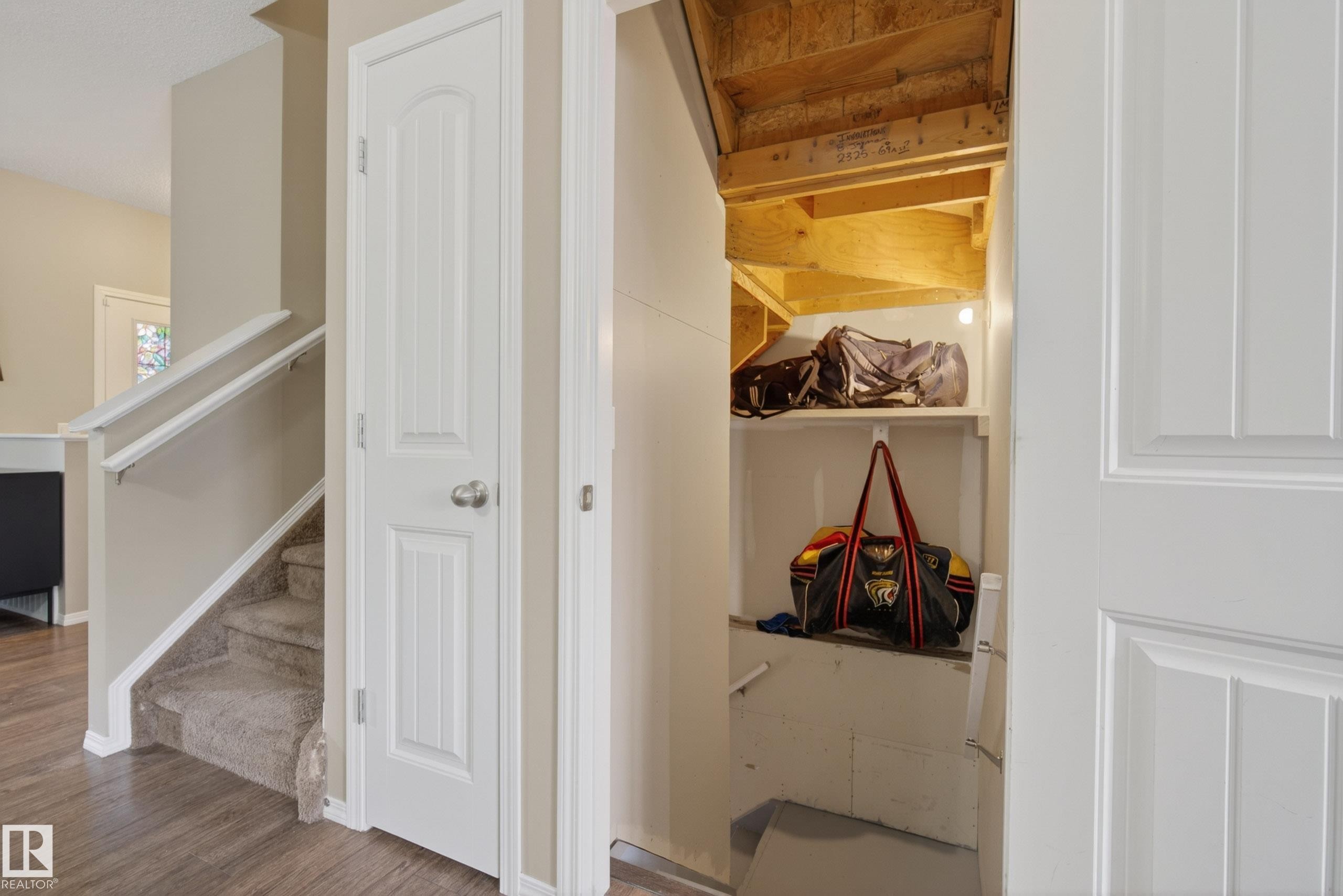 Under-stair storage area with shelving, adjacent to a carpeted staircase with white railings, and wood-finish flooring - 2325 69A Street, Edmonton, AB