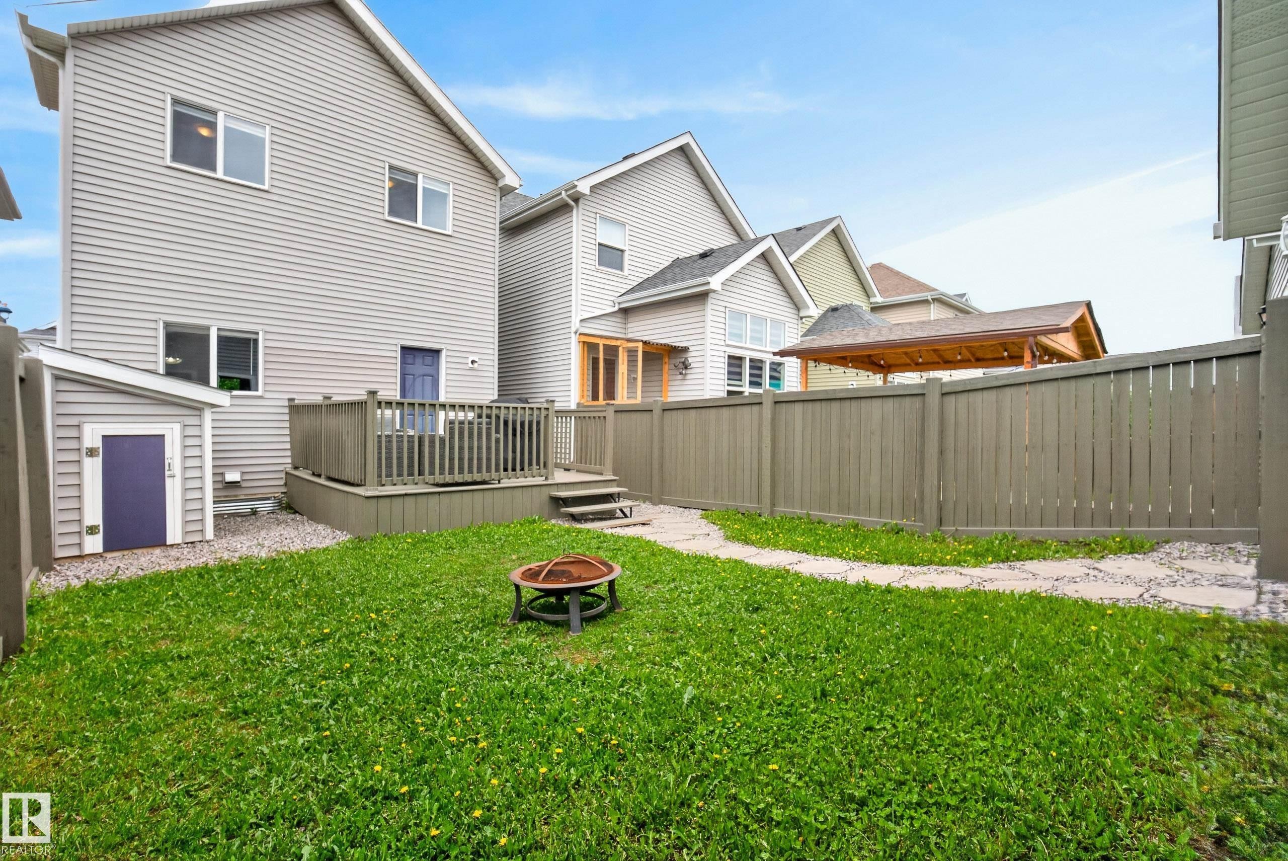 Expansive backyard featuring a manicured lawn, stone pathway, privacy fence, and a multi-level deck with railings - 2325 69A Street, Edmonton, AB