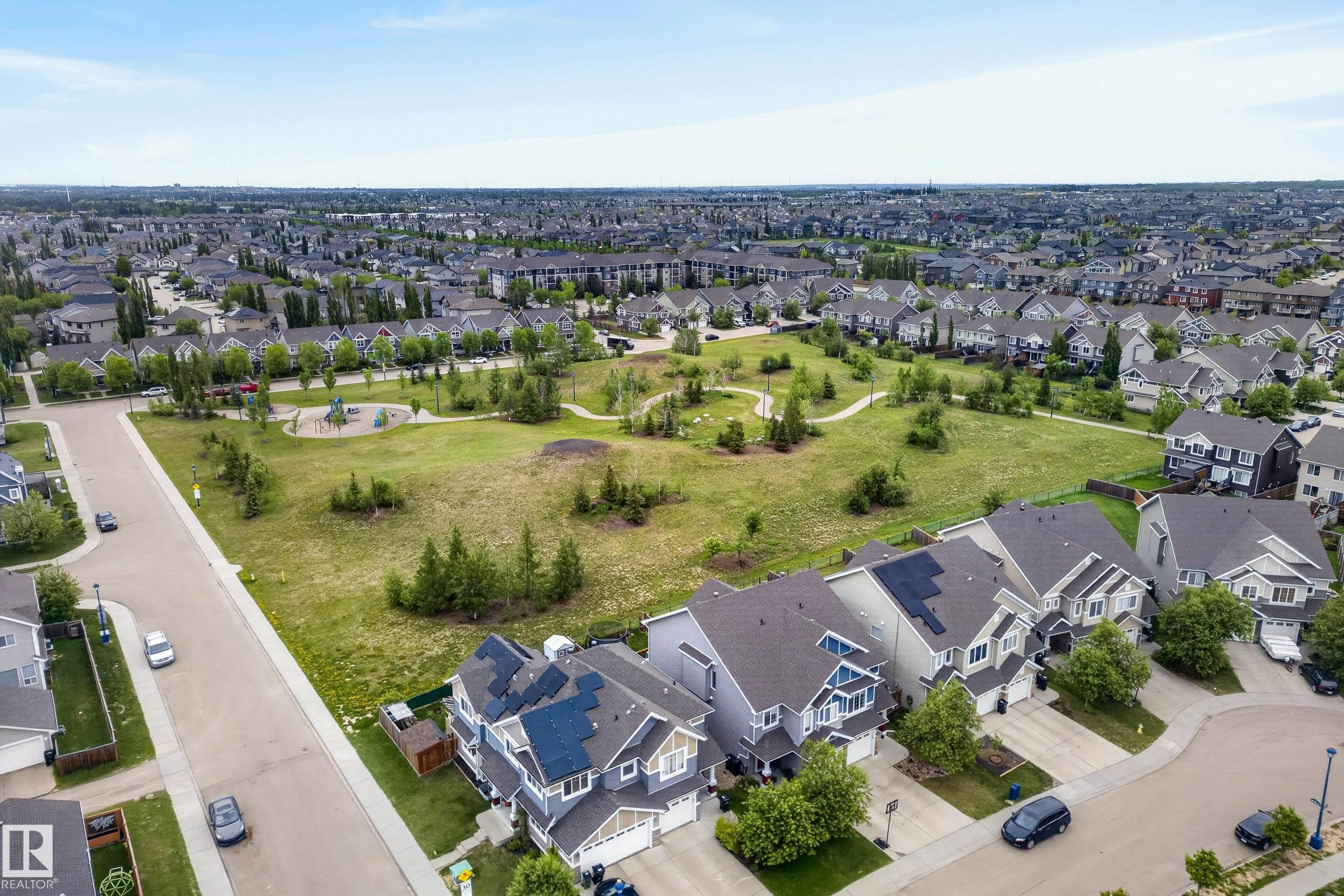Expansive open green space featuring a playground and walking paths, surrounded by a residential street and properties with solar panel installations - 2325 69A Street, Edmonton, AB