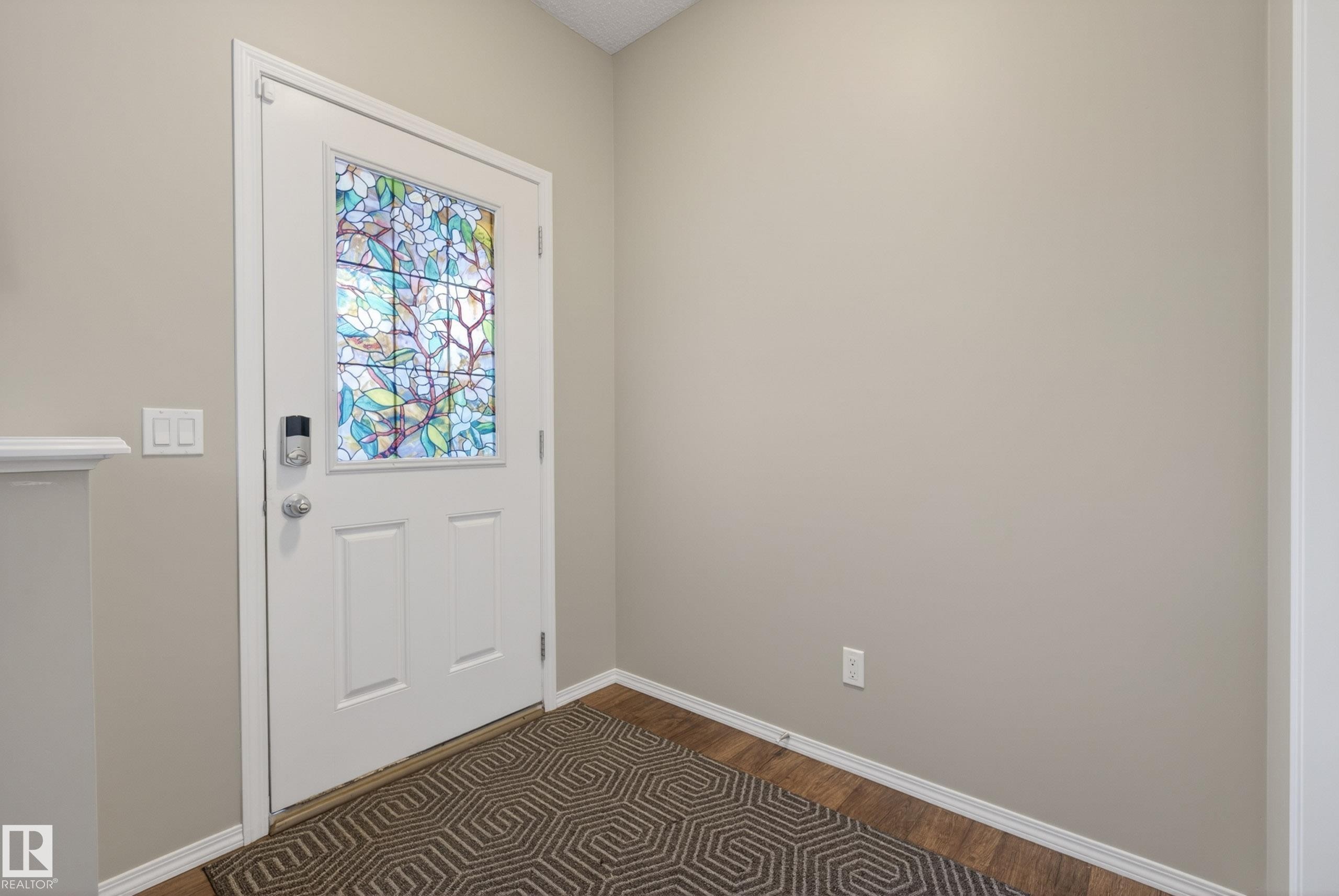Entryway featuring a white door with a stained-glass panel and smart lock, neutral painted walls, and wood-finish flooring - 2325 69A Street, Edmonton, AB