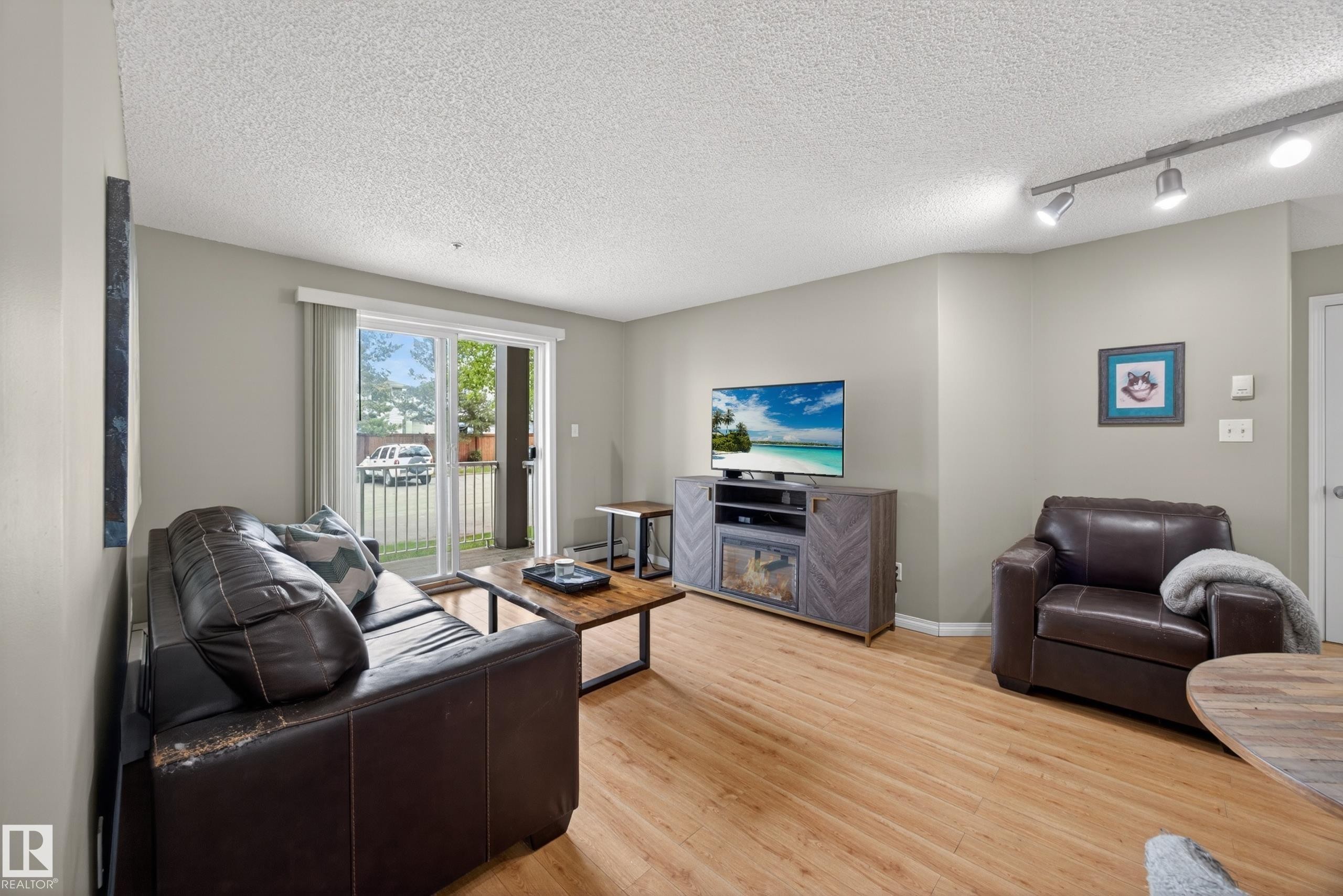 Living area featuring wood-finish flooring, light gray walls, and a sliding glass door providing access to an outdoor balcony - 111 3425 19, Edmonton, AB