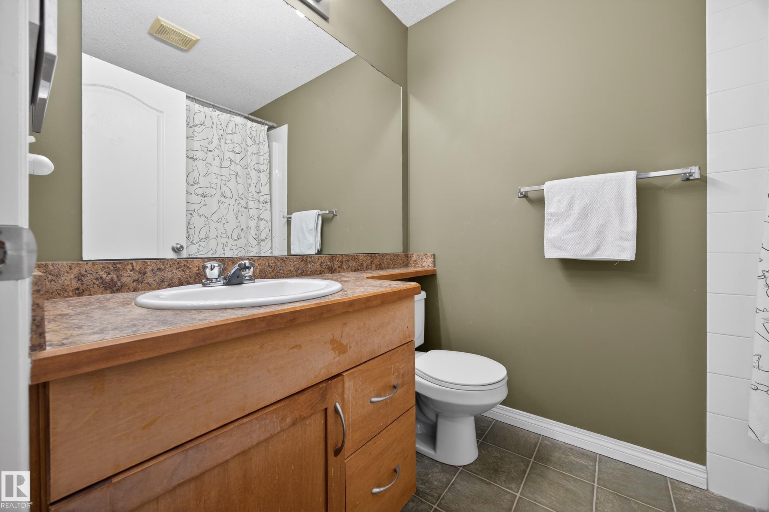 Bathroom featuring a light wood-finish vanity with an integrated basin, a stone-look countertop, an expansive wall mirror, and neutral wall paint - 111 3425 19, Edmonton, AB