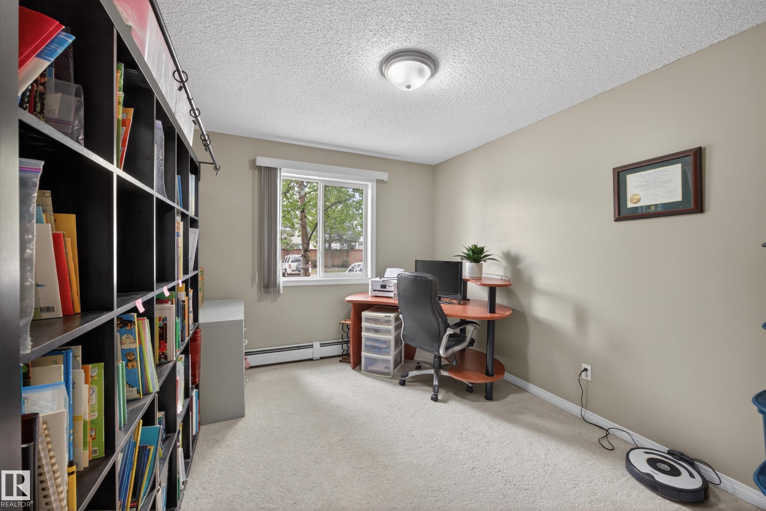 Room featuring light-toned carpeting, a window with a white frame, and a built-in black shelving unit - 111 3425 19, Edmonton, AB