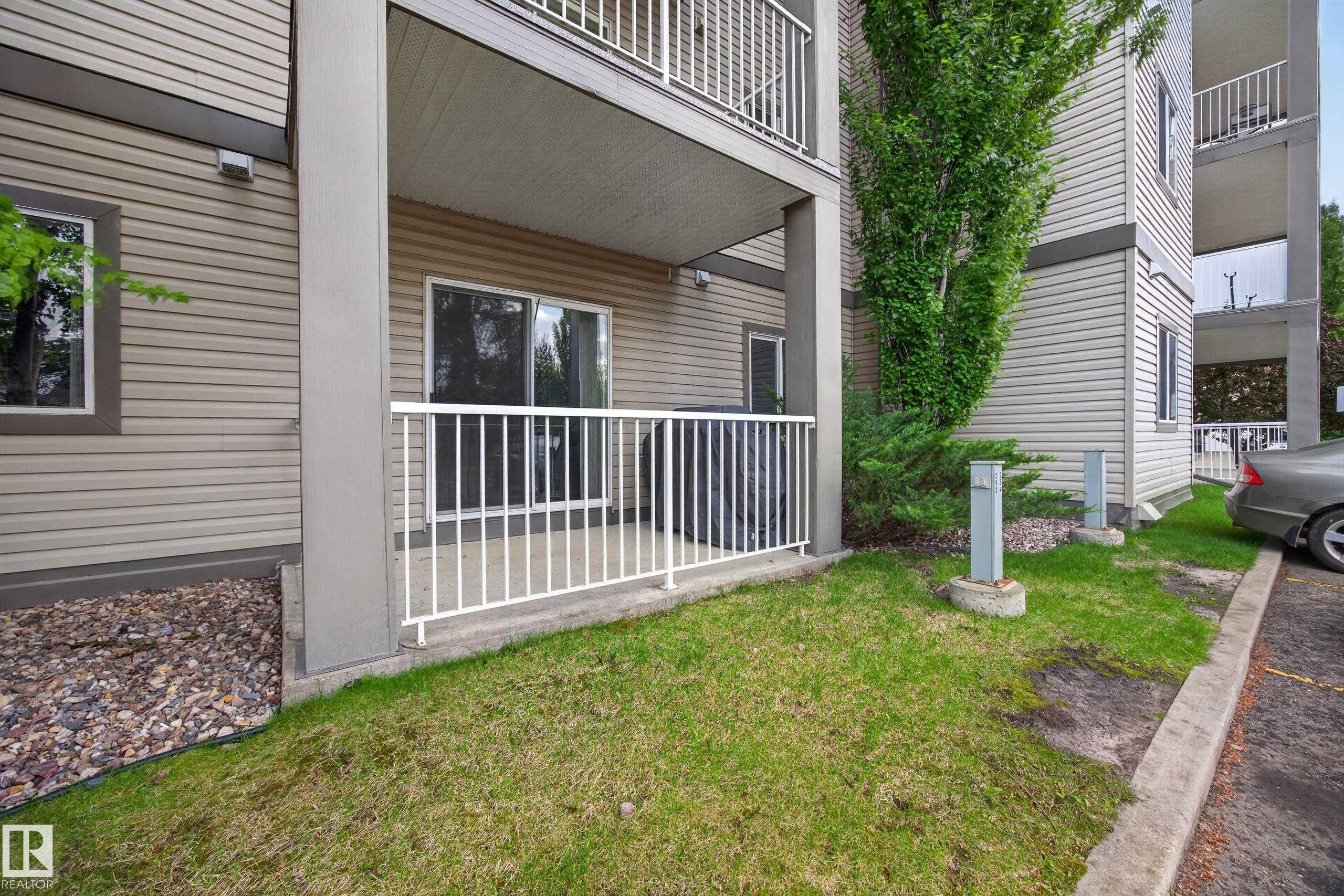 Ground-level patio with a white metal railing, featuring a sliding glass door entry, horizontal siding exterior, and adjacent green space - 111 3425 19, Edmonton, AB