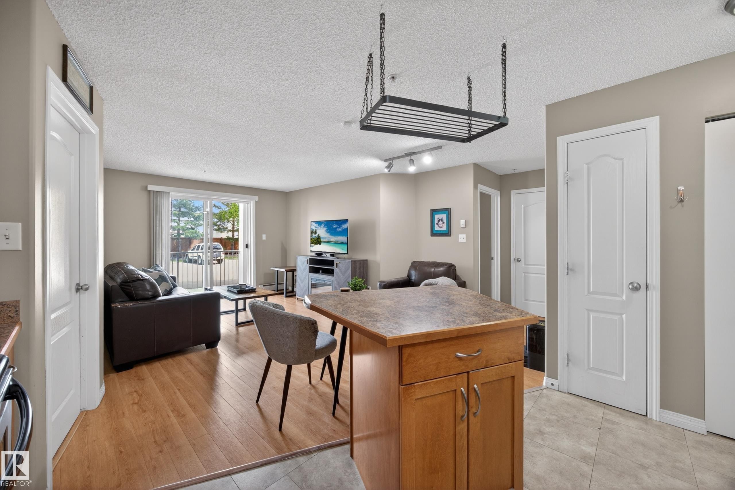 Open-concept living area featuring wood-finish flooring, a sliding glass door to an exterior space, and track lighting - 111 3425 19, Edmonton, AB