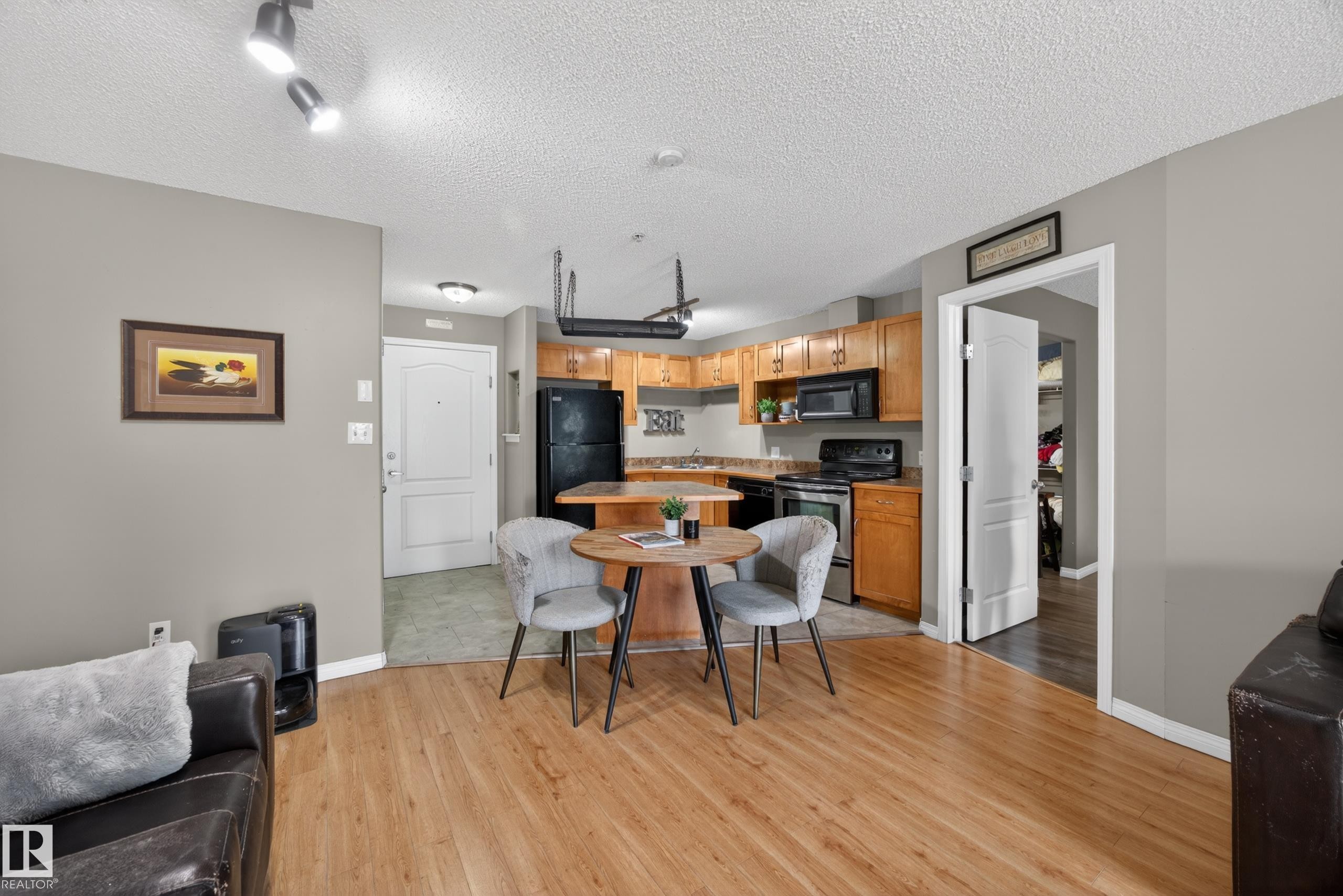 Kitchen and living area featuring wood-finish flooring, light wood cabinetry, black appliances, and track lighting - 111 3425 19, Edmonton, AB