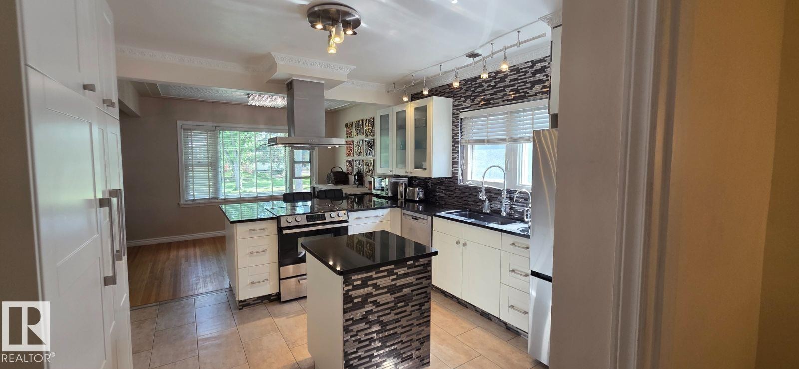 Modern kitchen featuring white cabinetry, black countertops, a mosaic tile backsplash, and stainless steel appliances - 6704 93 Street, Edmonton, AB