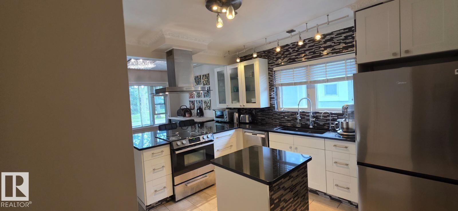 Modern kitchen featuring white cabinetry, dark countertops, and a mosaic tile backsplash - 6704 93 Street, Edmonton, AB