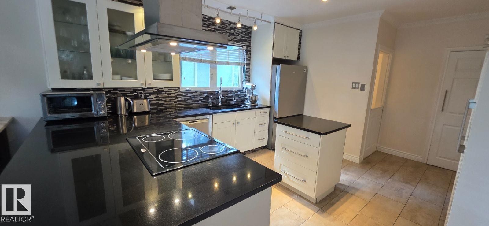 Kitchen featuring dark countertops, white cabinetry, a built-in cooktop, stainless steel appliances, and tile flooring - 6704 93 Street, Edmonton, AB