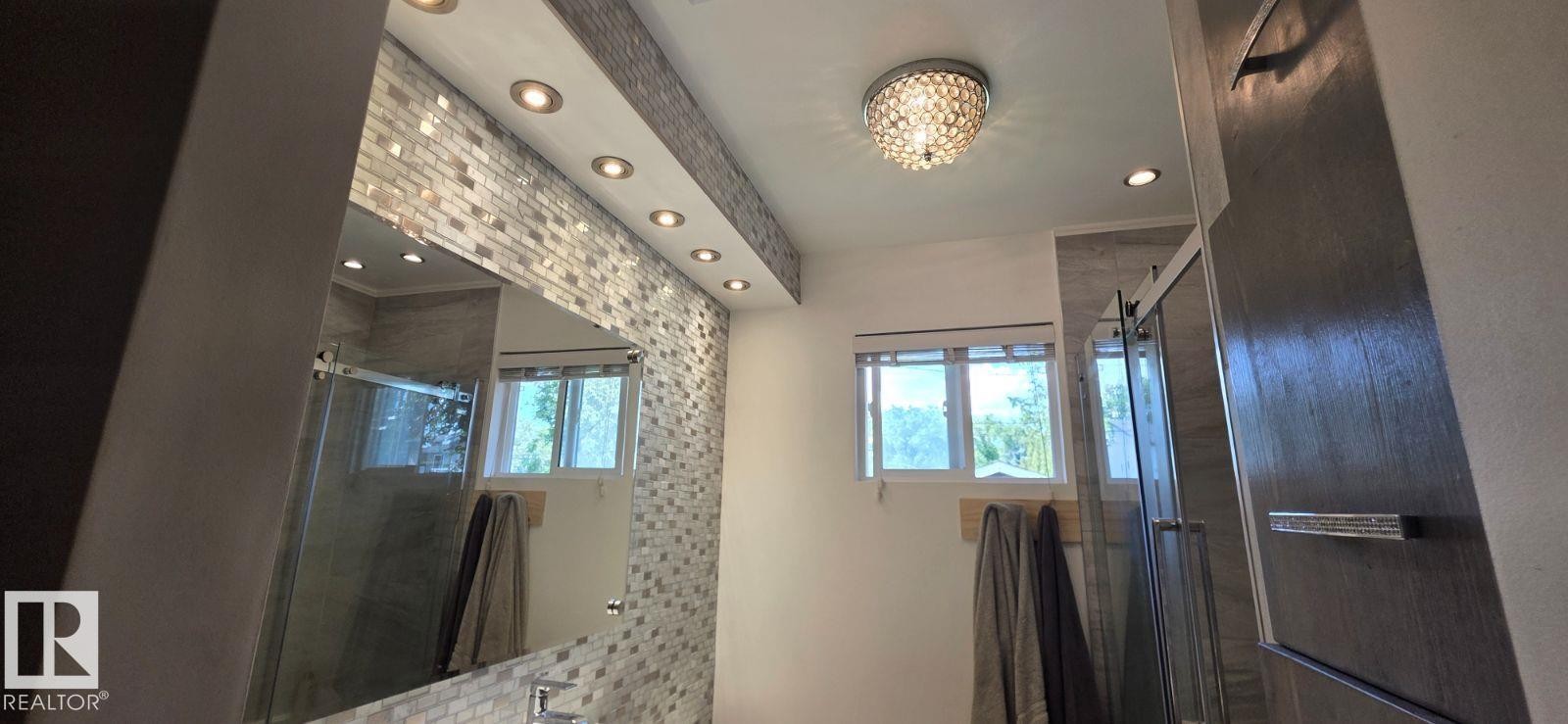 Contemporary bathroom featuring a crystal flush mount light fixture, recessed lighting, subway tile accent wall, and a glass-enclosed shower with sliding door - 6704 93 Street, Edmonton, AB