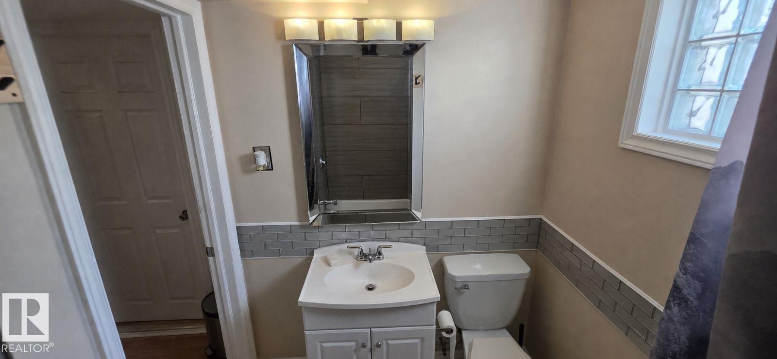Bathroom featuring a white vanity with integrated sink, rectangular medicine cabinet, and a four-light vanity fixture - 6704 93 Street, Edmonton, AB