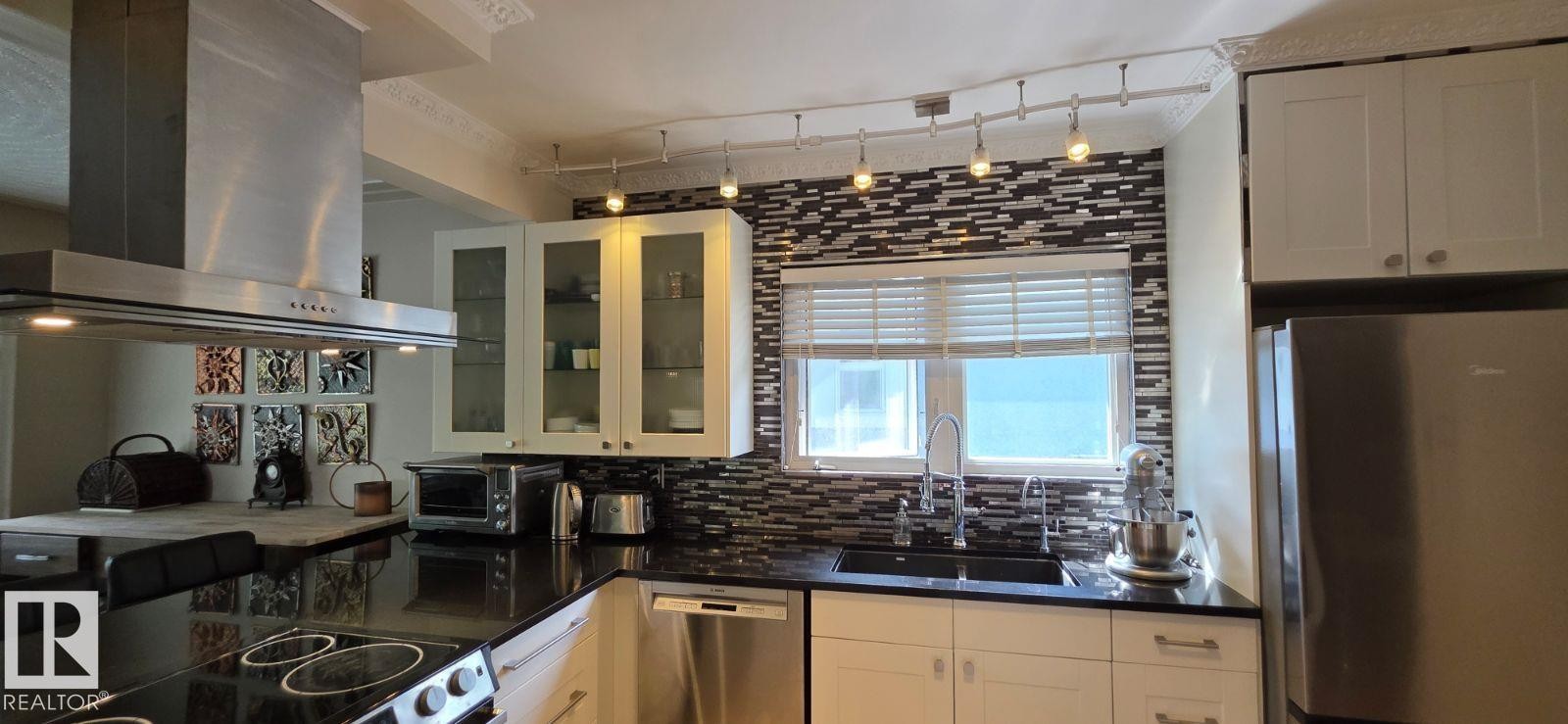 Modern kitchen with black countertops, a mosaic tile backsplash, and white cabinetry - 6704 93 Street, Edmonton, AB
