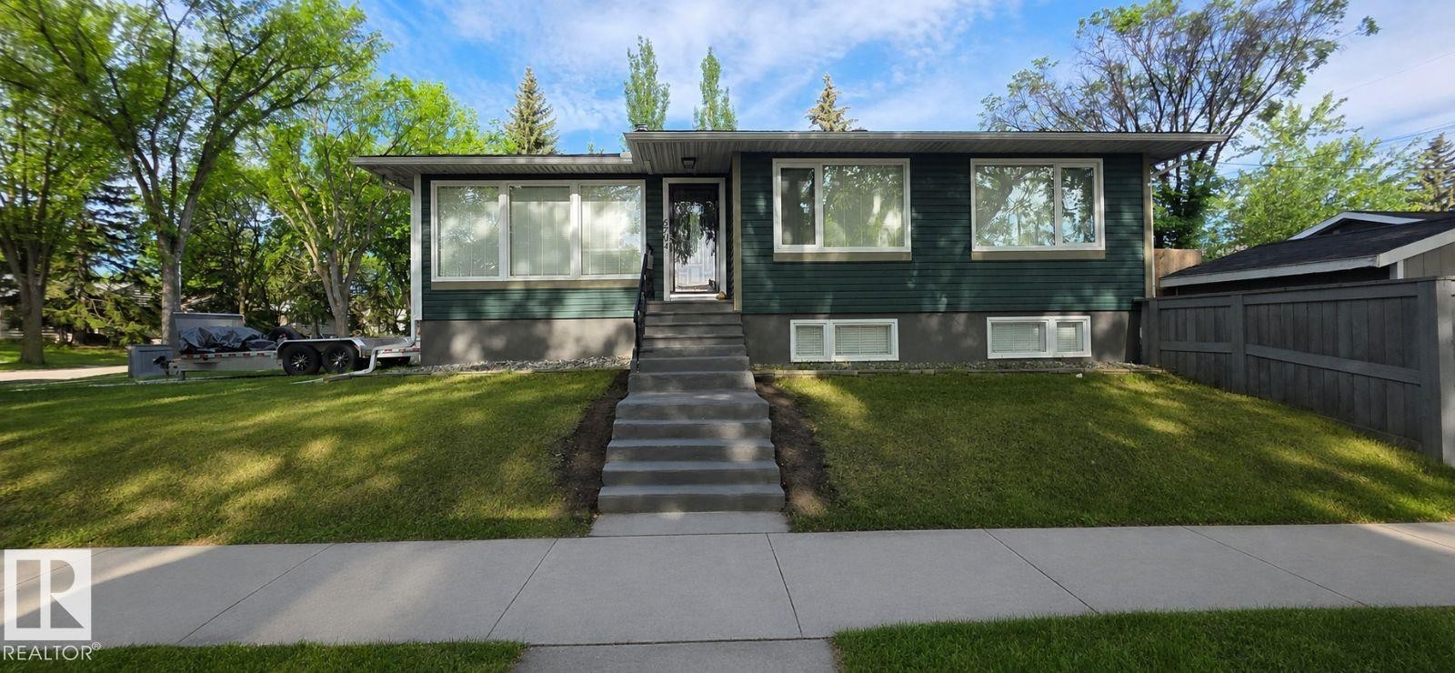 Split-level residence featuring a dark green exterior, white-framed windows, and a prominent front entrance with concrete steps - 6704 93 Street, Edmonton, AB