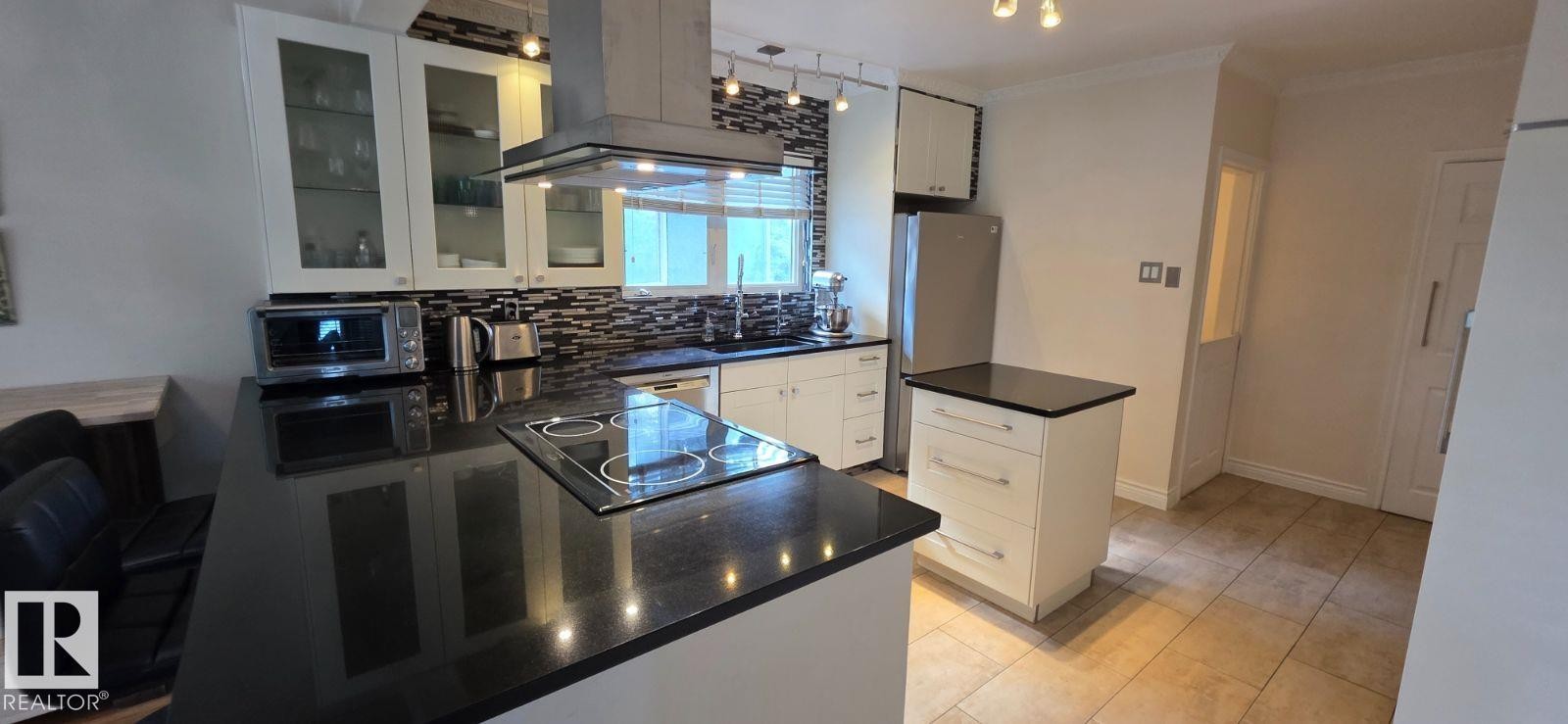 Kitchen featuring a built-in cooktop, stainless steel range hood, dark countertops, white cabinetry, and tile flooring - 6704 93 Street, Edmonton, AB
