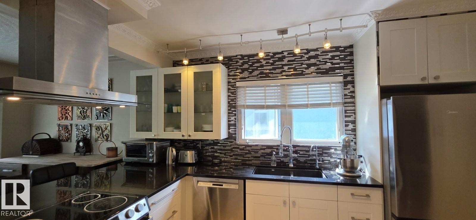 Modern kitchen with black countertops and a mosaic tile backsplash - 6704 93 Street, Edmonton, AB