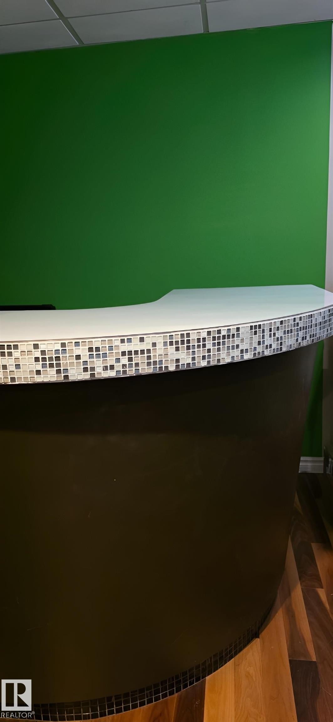 Curved reception desk featuring a tiled base, white countertop, and wood-finish flooring - 6704 93 Street, Edmonton, AB