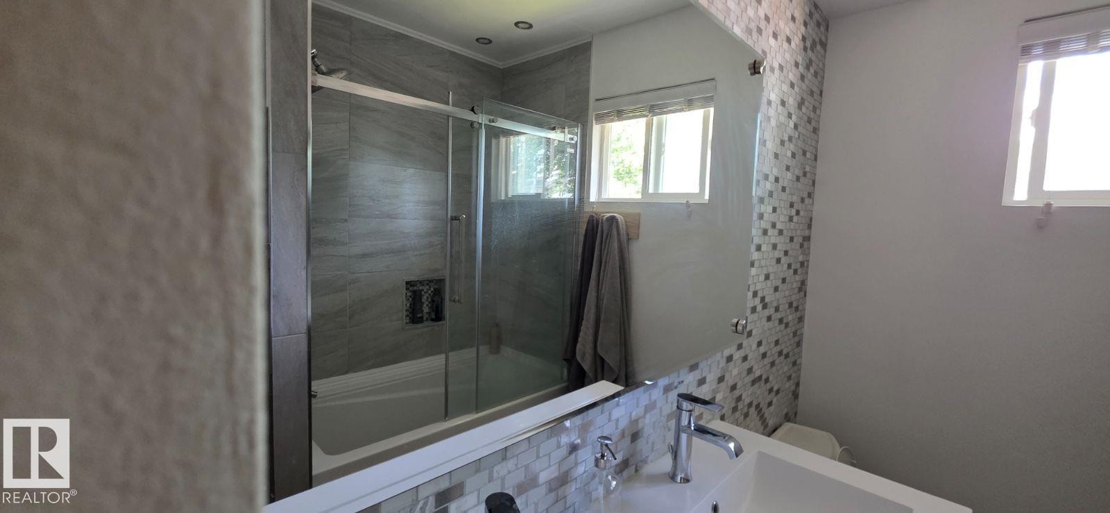 Bathroom featuring a vanity with a rectangular sink, chrome faucet, and mosaic tile backsplash - 6704 93 Street, Edmonton, AB