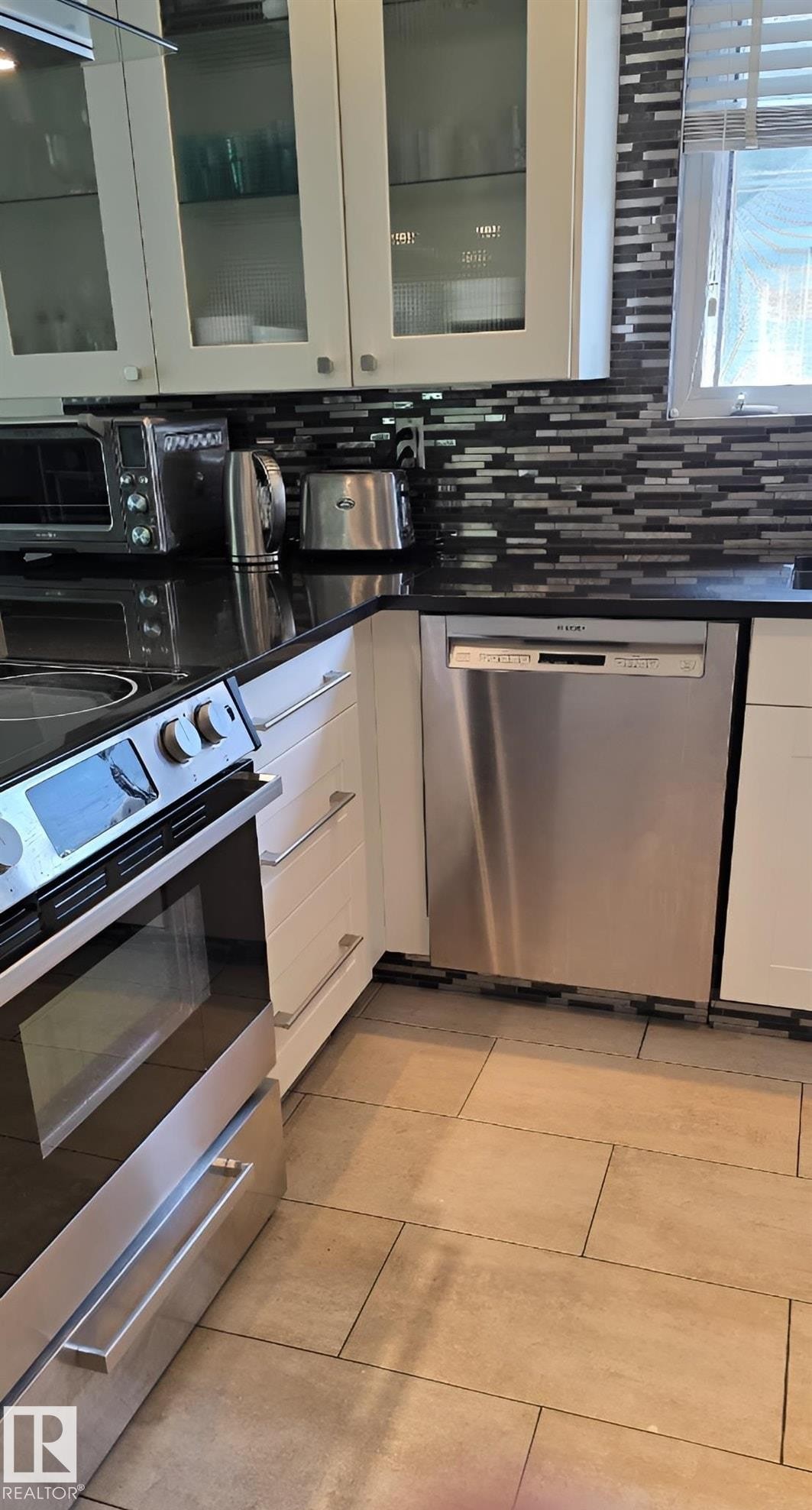 Contemporary kitchen featuring white cabinetry, a black countertop, a mosaic tile backsplash, stainless steel appliances, and large format floor tiling - 6704 93 Street, Edmonton, AB