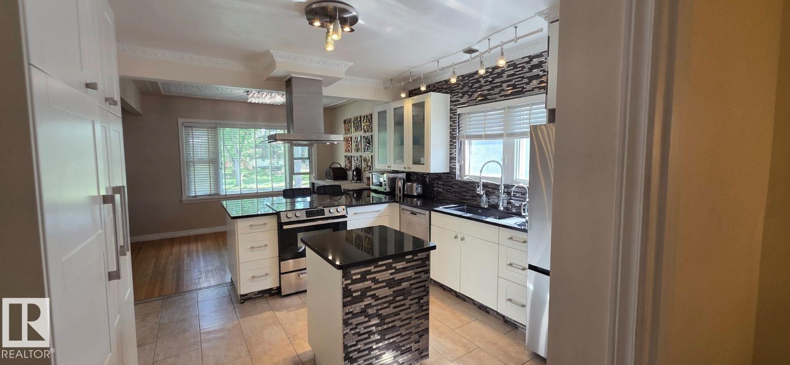 Kitchen featuring white cabinetry, black countertops, stainless steel appliances, a tiled backsplash, and recessed lighting - 6704 93 Street, Edmonton, AB