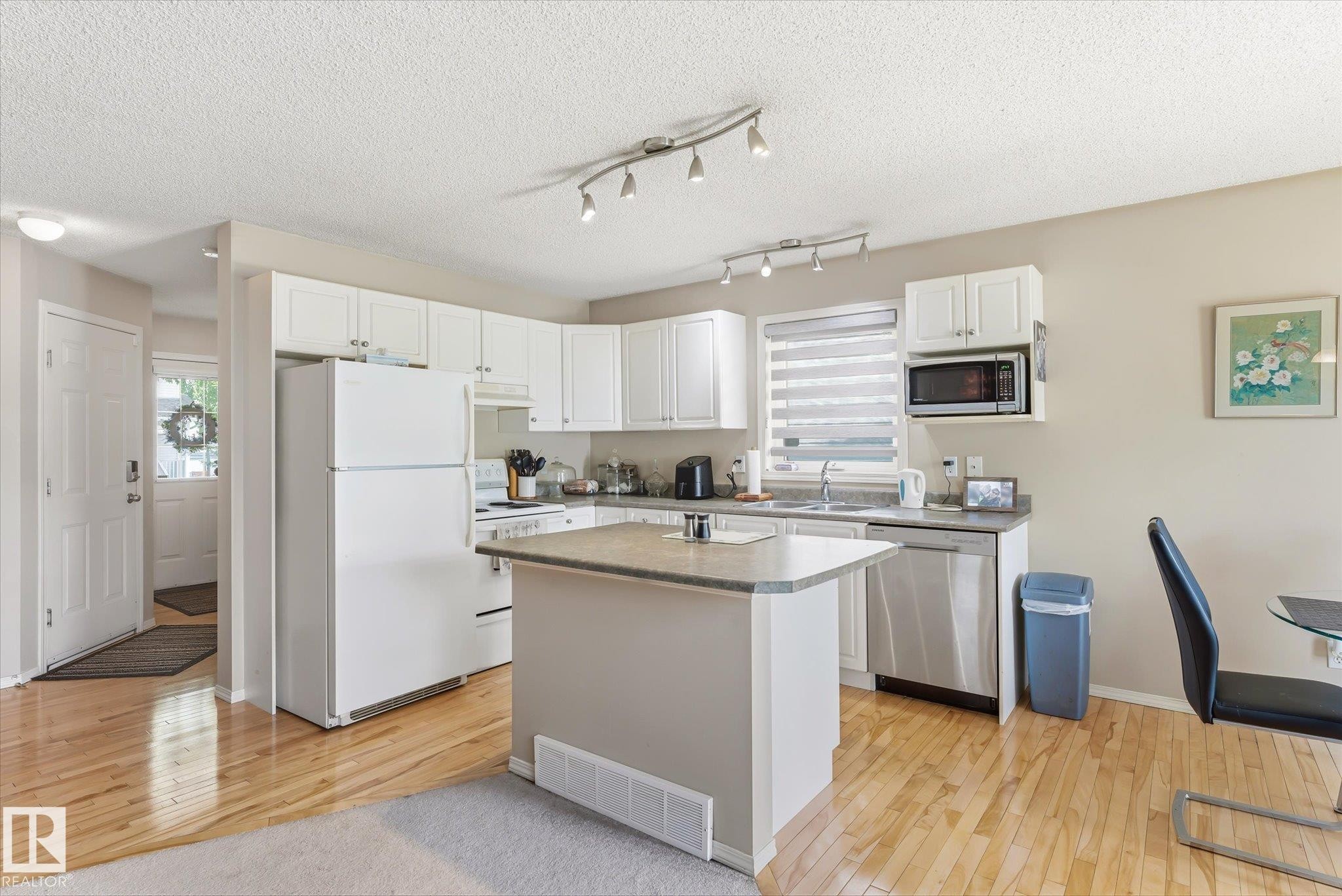 Kitchen featuring white cabinetry, a central island, stainless steel dishwasher, and wood-finish flooring - #37 4020 21 St Nw, Edmonton, AB - Indoor Photo Showing Kitchen