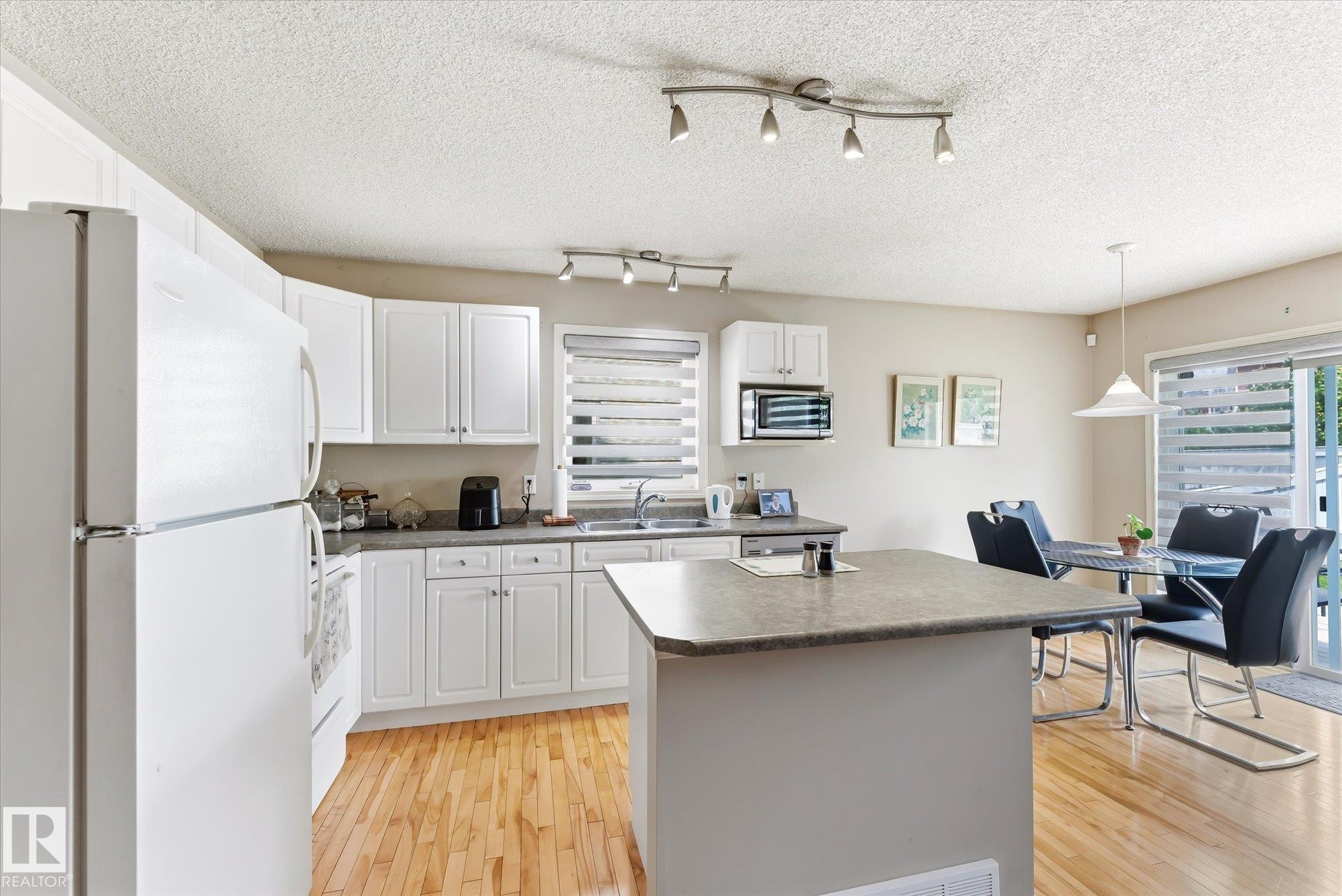 Kitchen with wood-finish flooring, white cabinetry, track lighting, and a kitchen island - #37 4020 21 St Nw, Edmonton, AB - Indoor Photo Showing Kitchen With Double Sink
