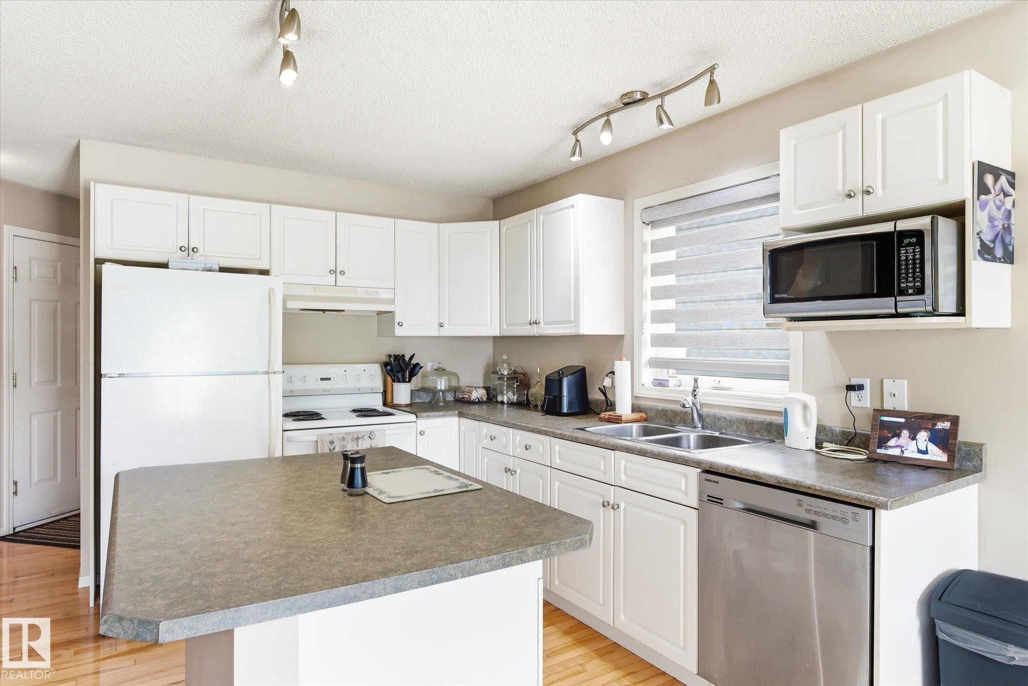 Kitchen featuring white cabinetry, track lighting, and wood-finish flooring - #37 4020 21 St Nw, Edmonton, AB - Indoor Photo Showing Kitchen With Double Sink
