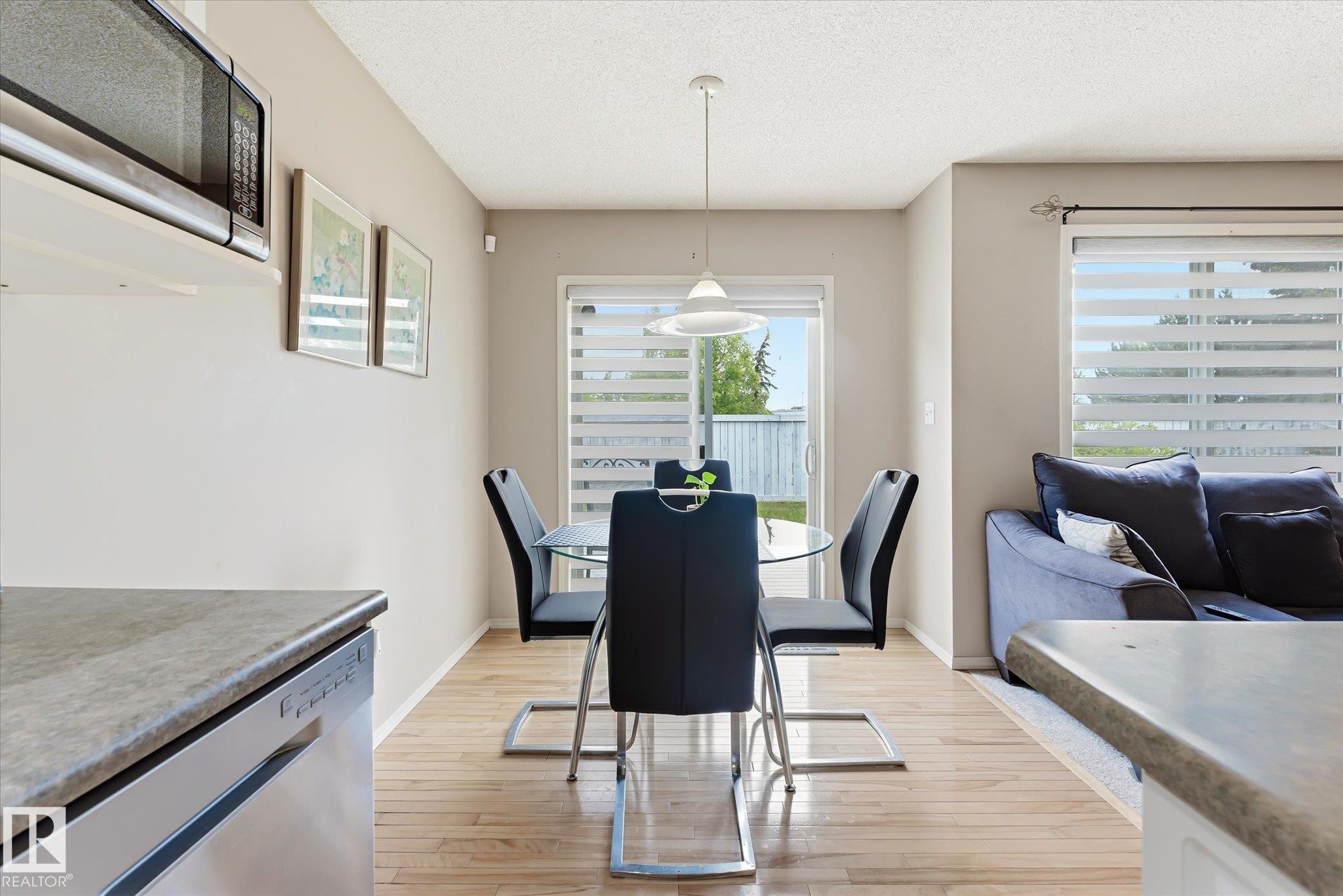 Open concept dining area featuring wood-finish flooring, a contemporary pendant light fixture, and a sliding glass door with horizontal blinds - #37 4020 21 St Nw, Edmonton, AB - Indoor Photo Showing Dining Room