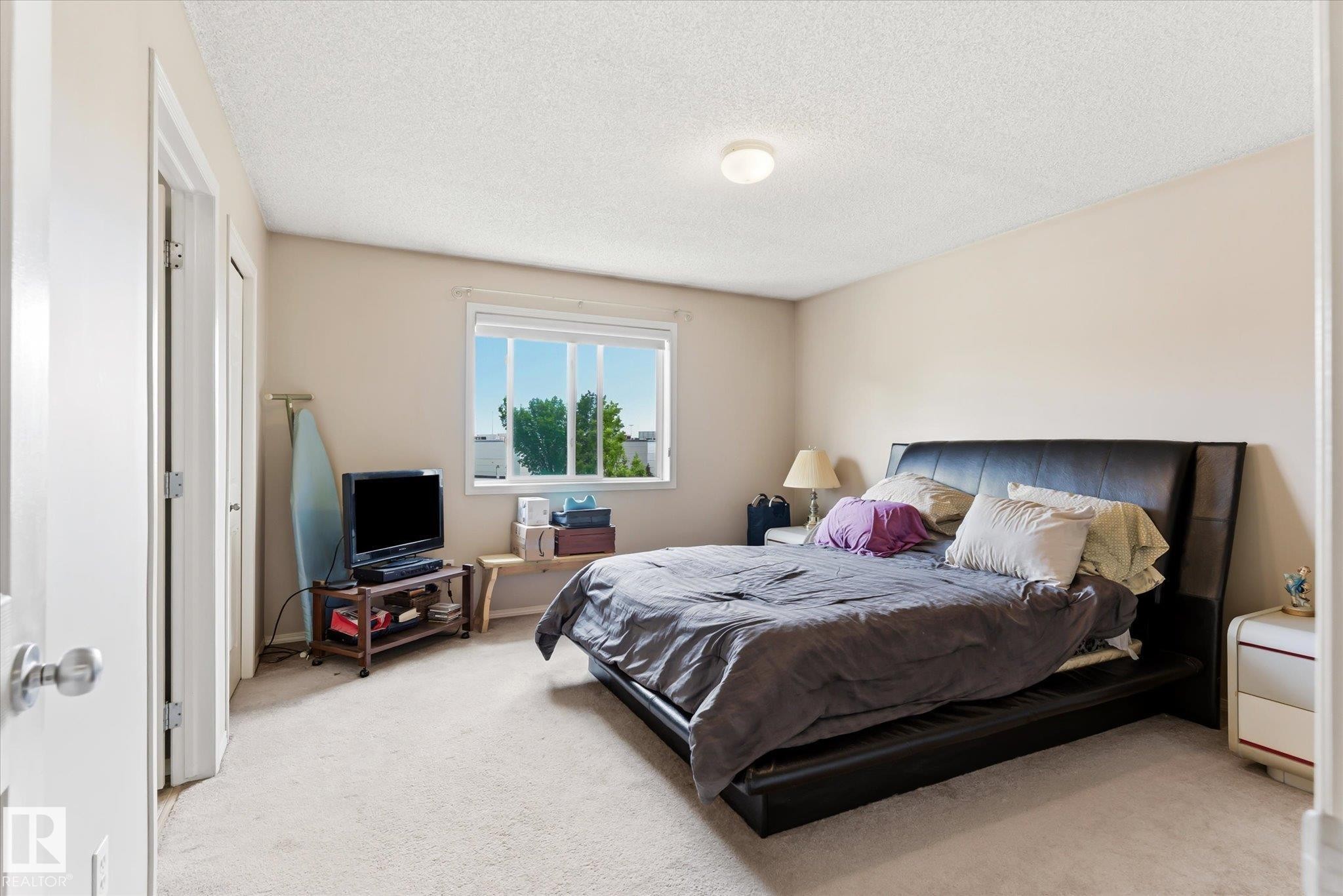 Carpeted bedroom with a single overhead flush-mount light fixture, two white bi-fold closet doors, a single window, and neutral-toned wall paint - #37 4020 21 St Nw, Edmonton, AB - Indoor Photo Showing Bedroom