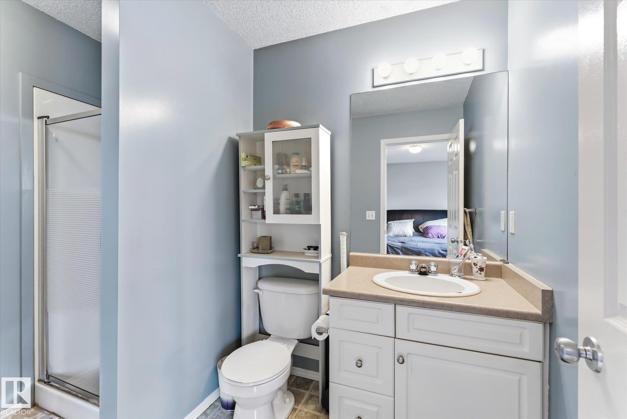 Bathroom featuring a glass-enclosed shower, white vanity with integrated sink, light-toned countertop, and overhead mirror with strip lighting - #37 4020 21 St Nw, Edmonton, AB - Indoor Photo Showing Bathroom