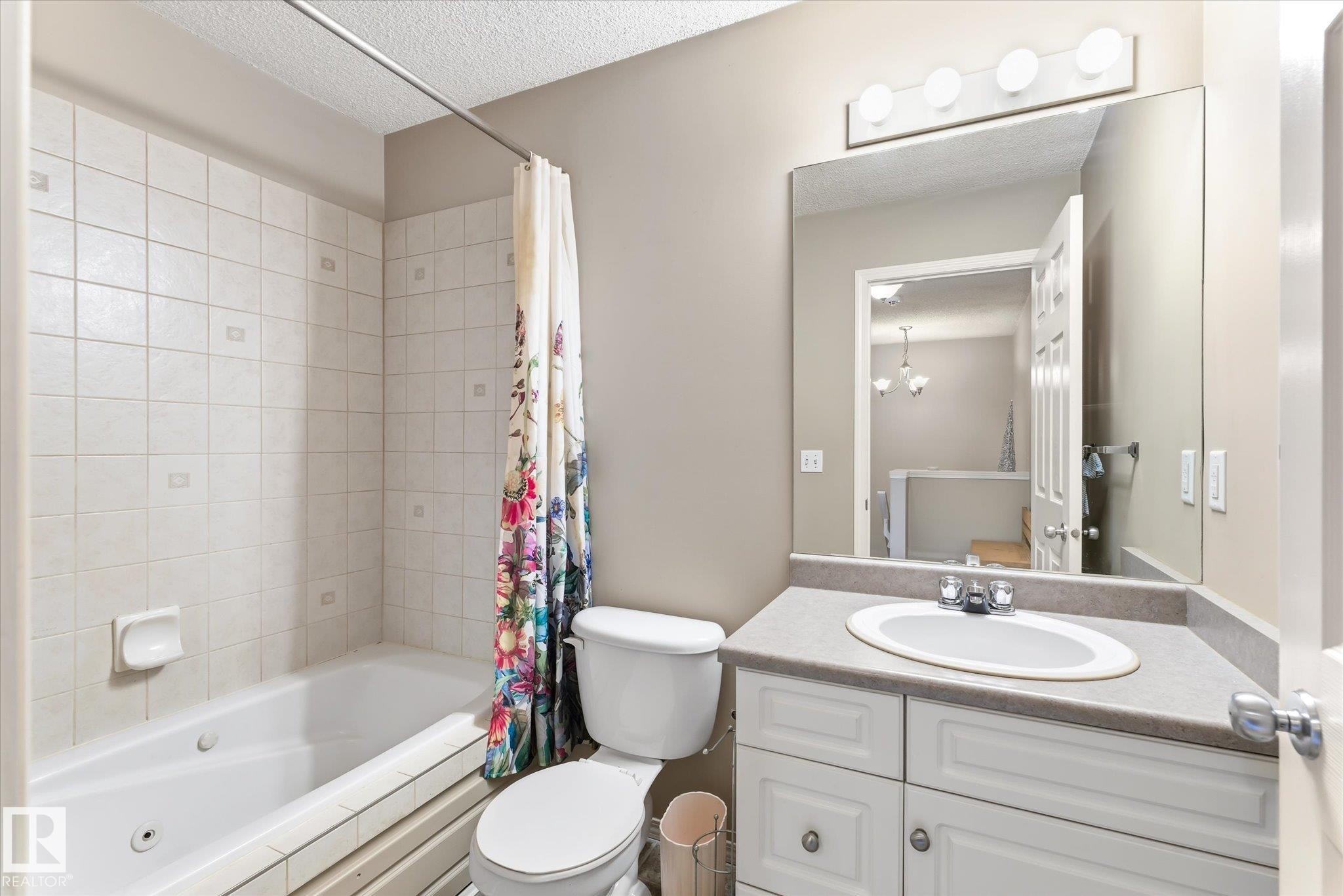 Bathroom featuring a built-in tub with tile surround, white vanity with integrated sink, chrome faucet, and overhead vanity lighting - #37 4020 21 St Nw, Edmonton, AB - Indoor Photo Showing Bathroom