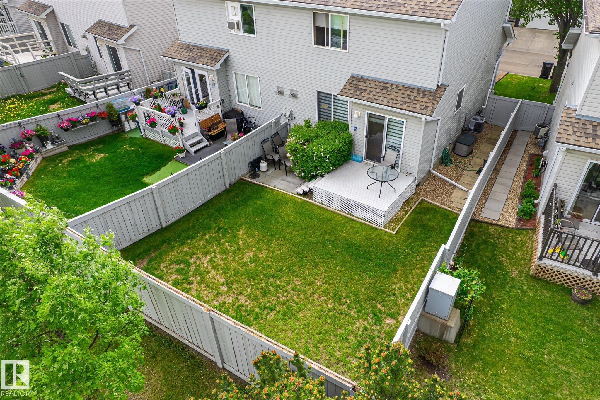 Private backyard featuring a manicured lawn, a grey wooden fence, and a dedicated patio area - #37 4020 21 St Nw, Edmonton, AB - Outdoor With Exterior