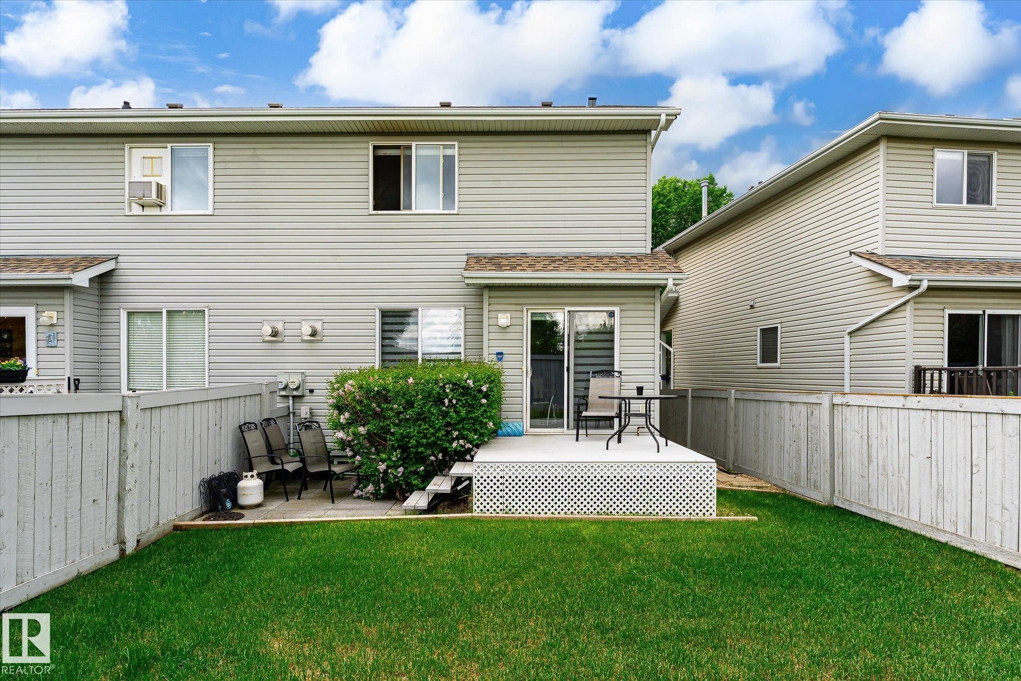 Fenced backyard featuring a manicured lawn, a raised deck with lattice skirting, and a sliding glass door for patio access - #37 4020 21 St Nw, Edmonton, AB - Outdoor With Exterior