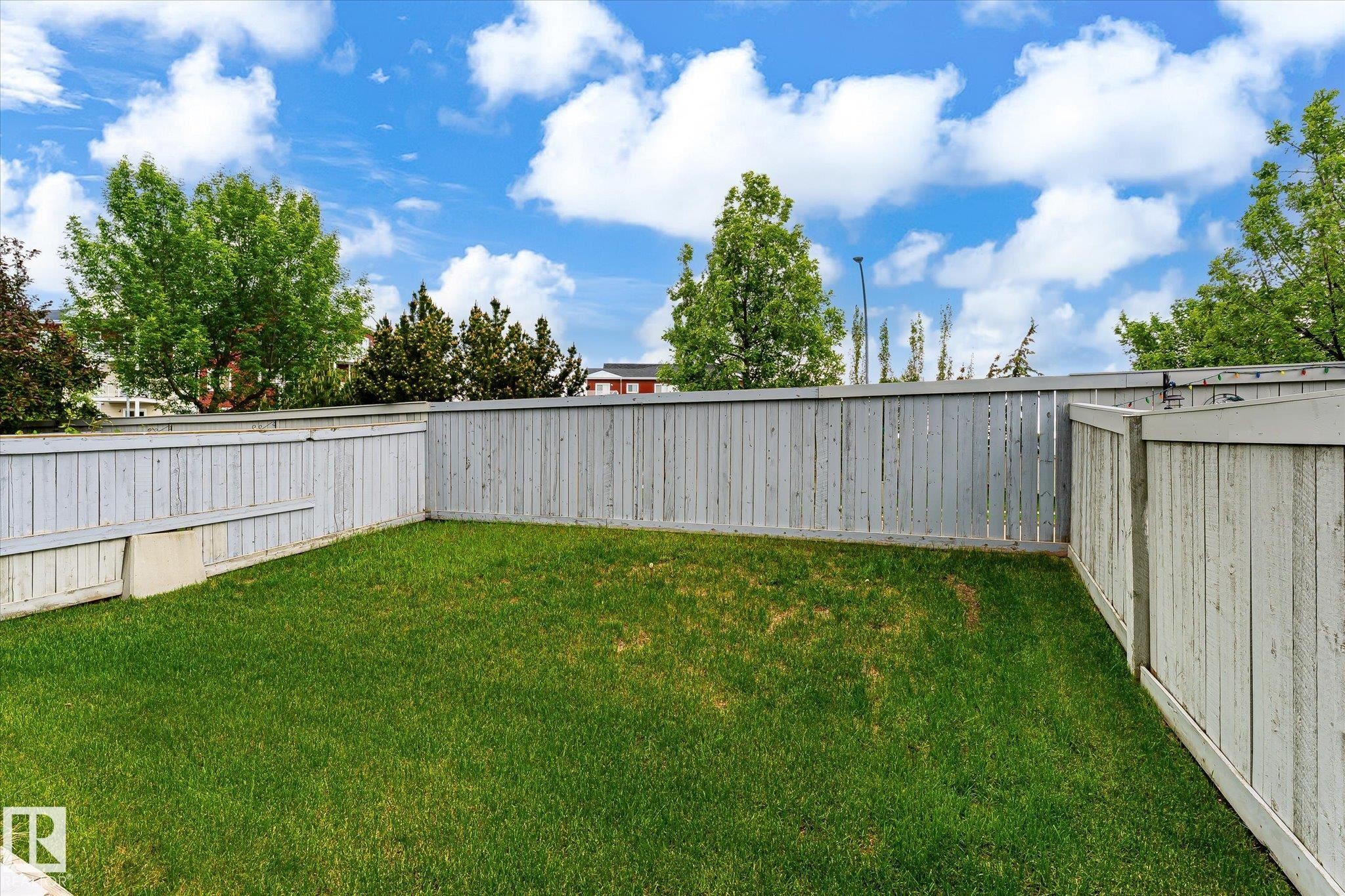 Expansive yard featuring a manicured lawn, full perimeter privacy fencing, and mature trees beyond - #37 4020 21 St Nw, Edmonton, AB - Outdoor