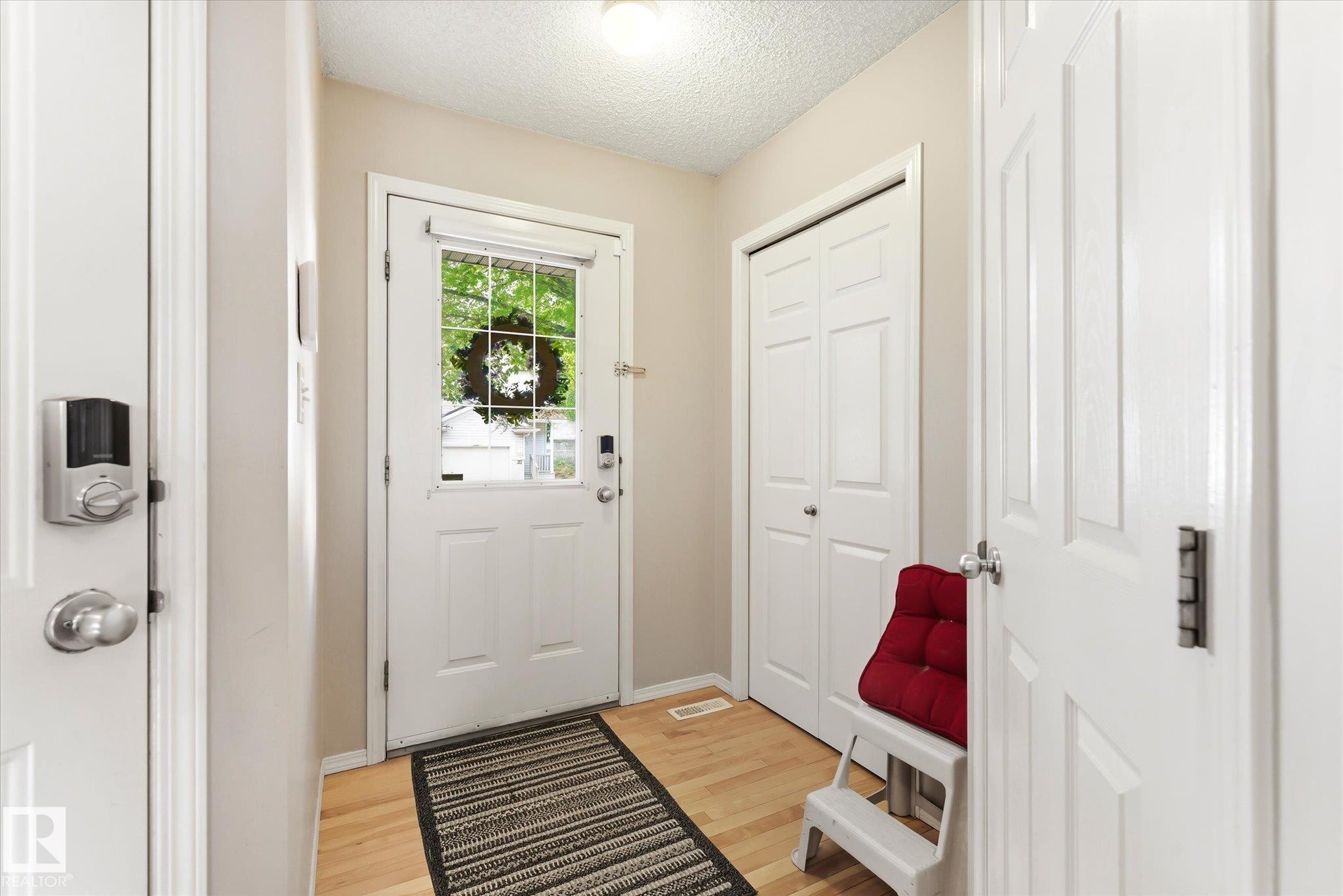 Entryway featuring light wood-finish flooring, a white front door with an integrated glass panel, a smart lock system, and bi-fold closet doors - #37 4020 21 St Nw, Edmonton, AB - Indoor Photo Showing Other Room